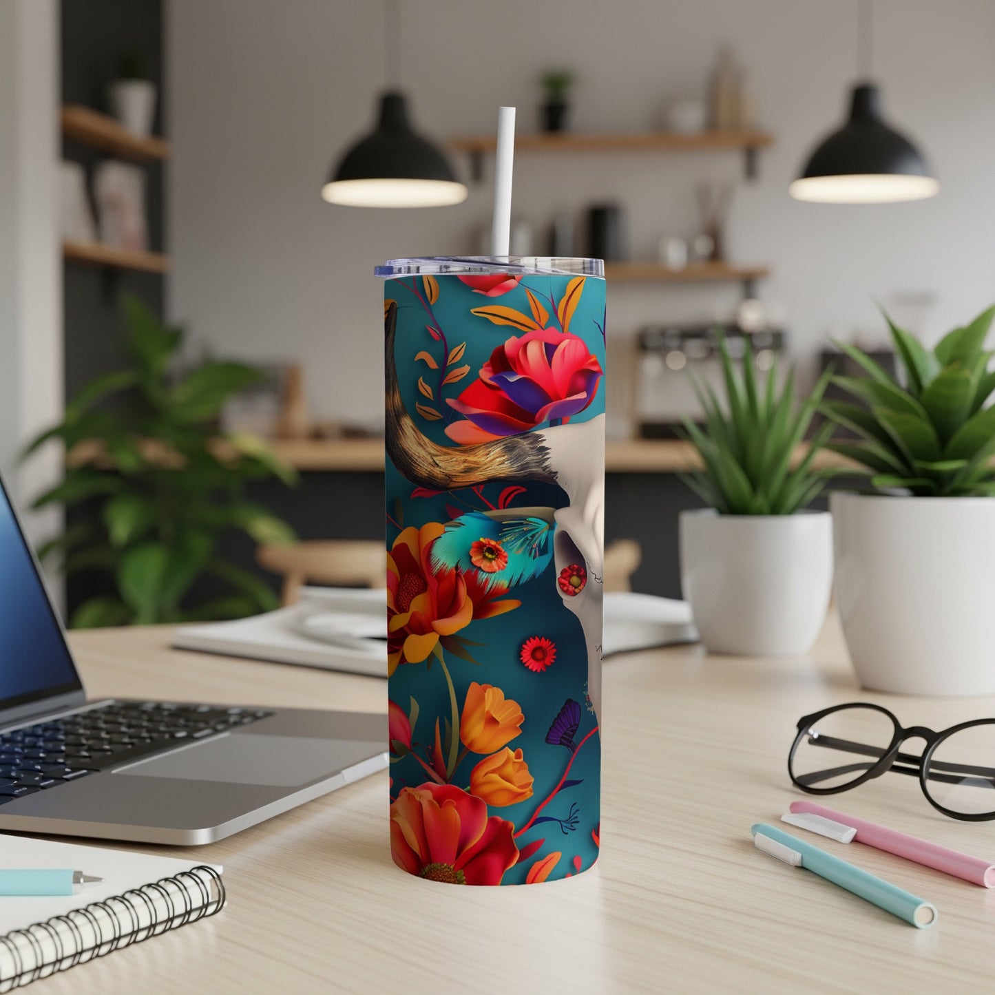 Tumbler with floral skull design and straw, on a desk.
