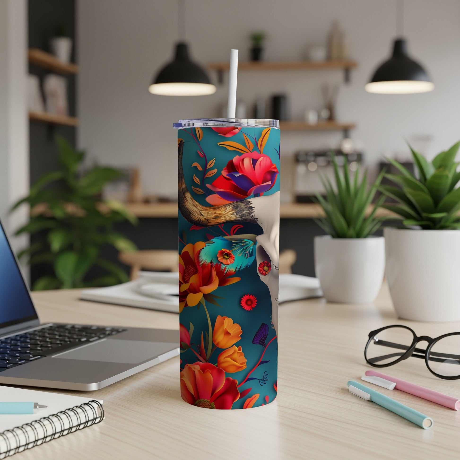 Tumbler with floral skull design and straw, on a desk.