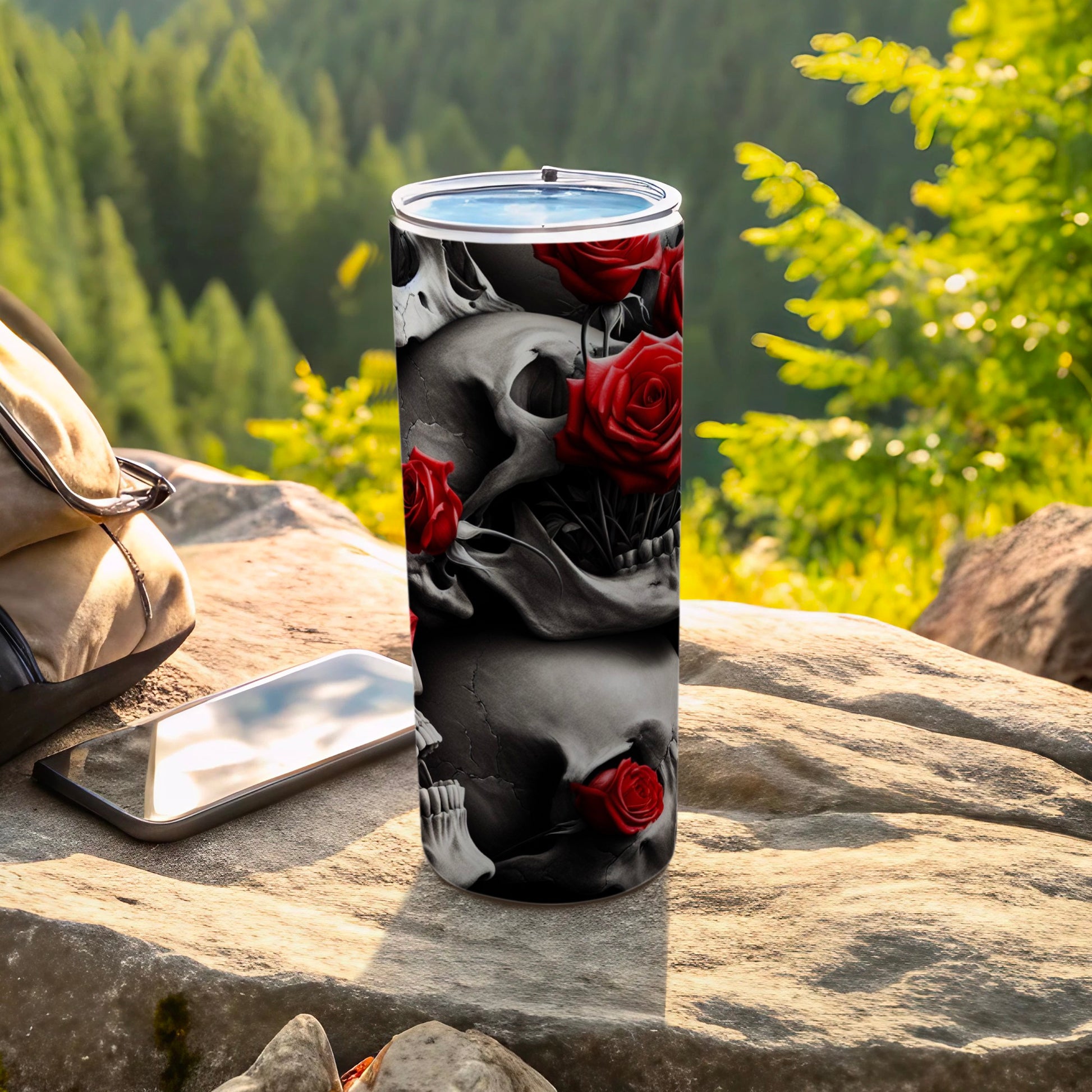 Skull and rose patterned tumbler on rock with backpack and phone.