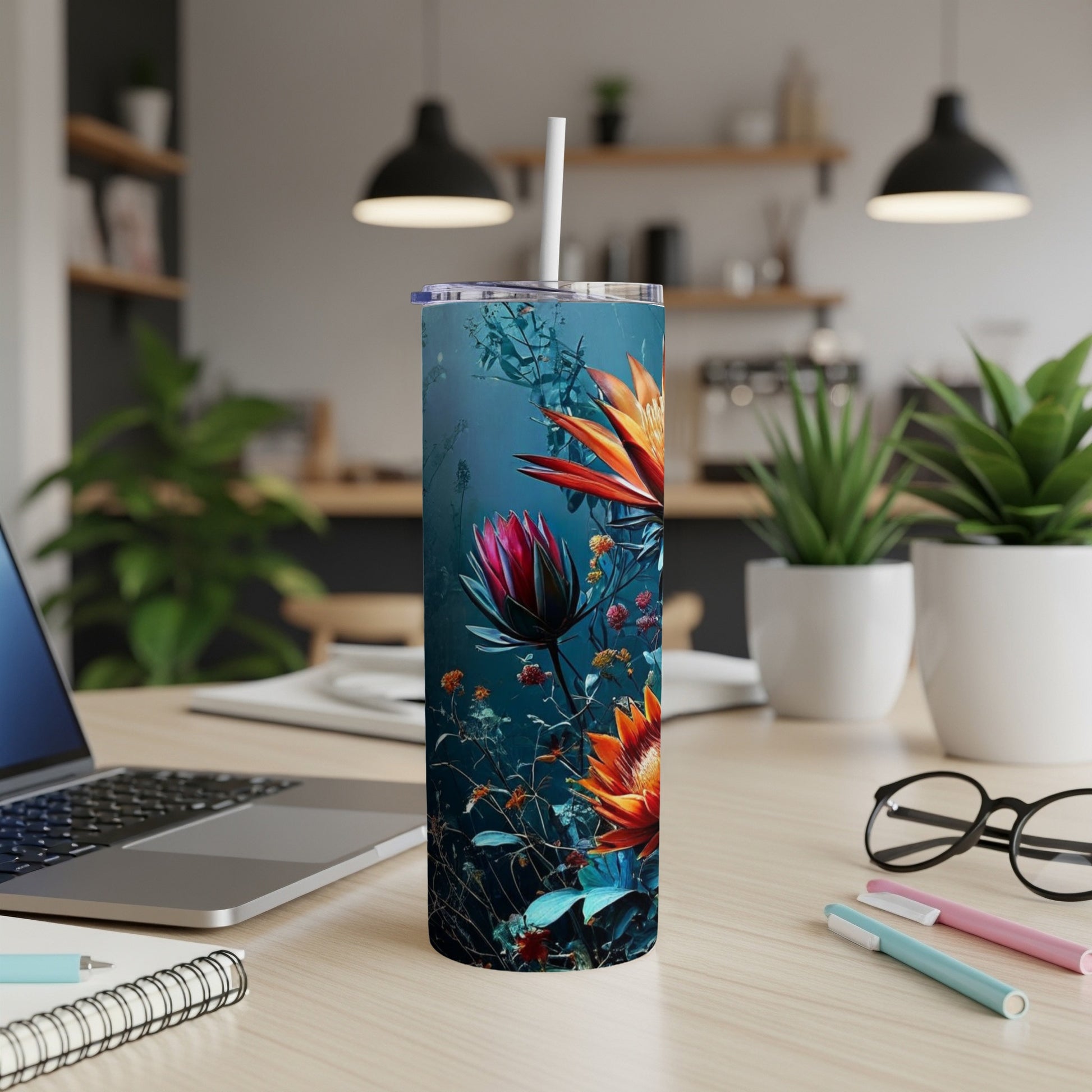 Floral tumbler with straw on a desk with a laptop and pens.
