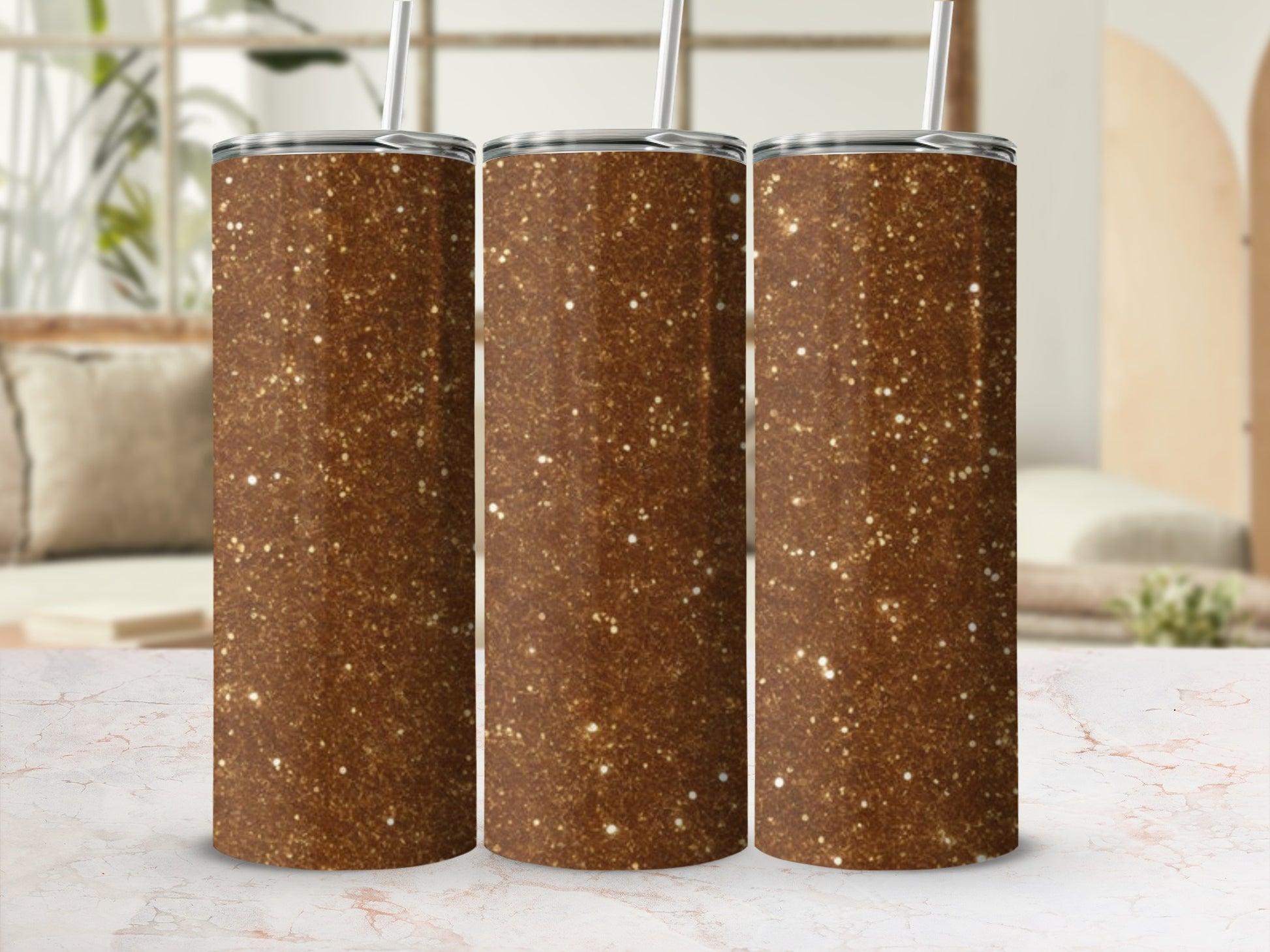 Three glittery brown tumblers with straws stand on a marbled surface.