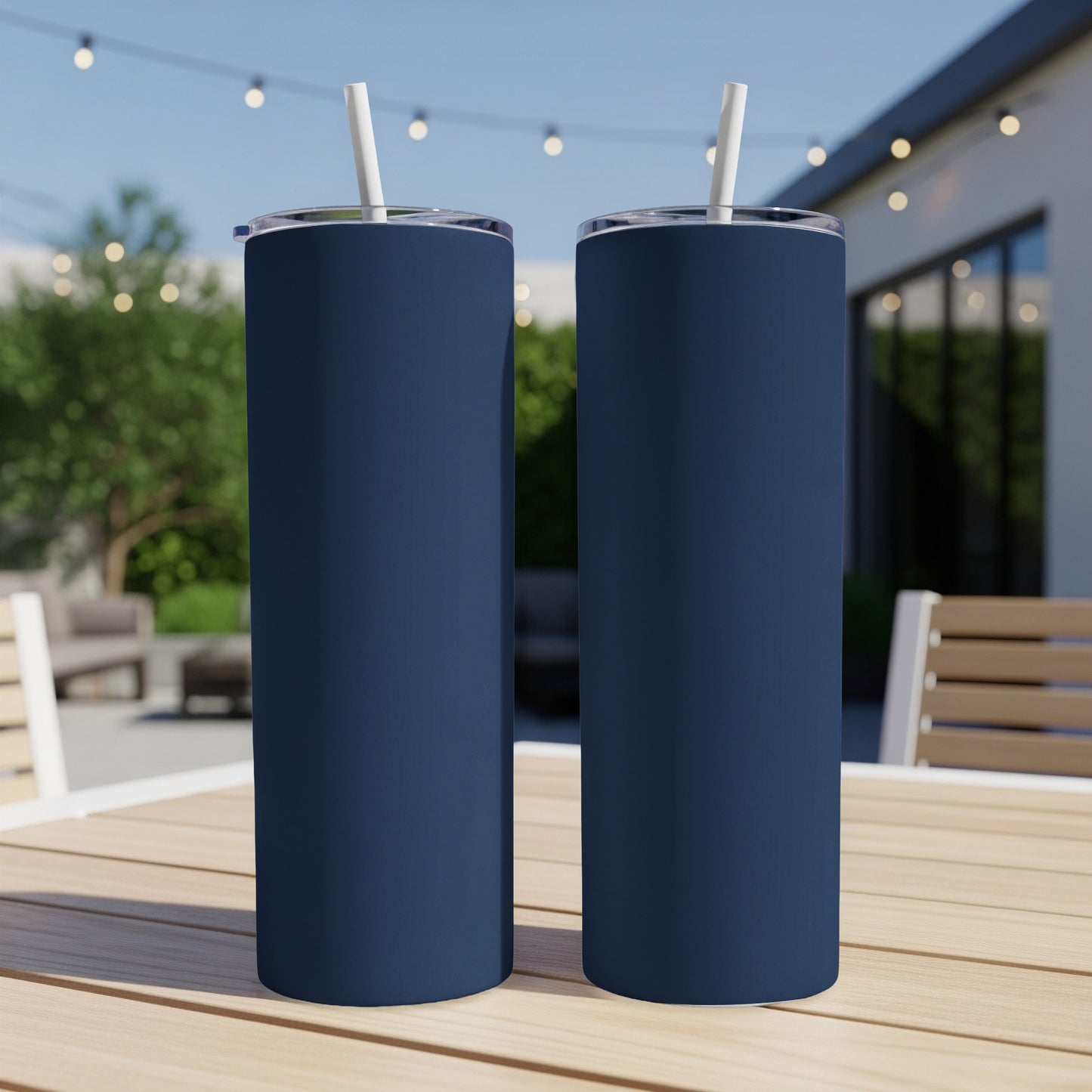 Two navy blue tumblers with white straws stand on a wooden table outdoors.