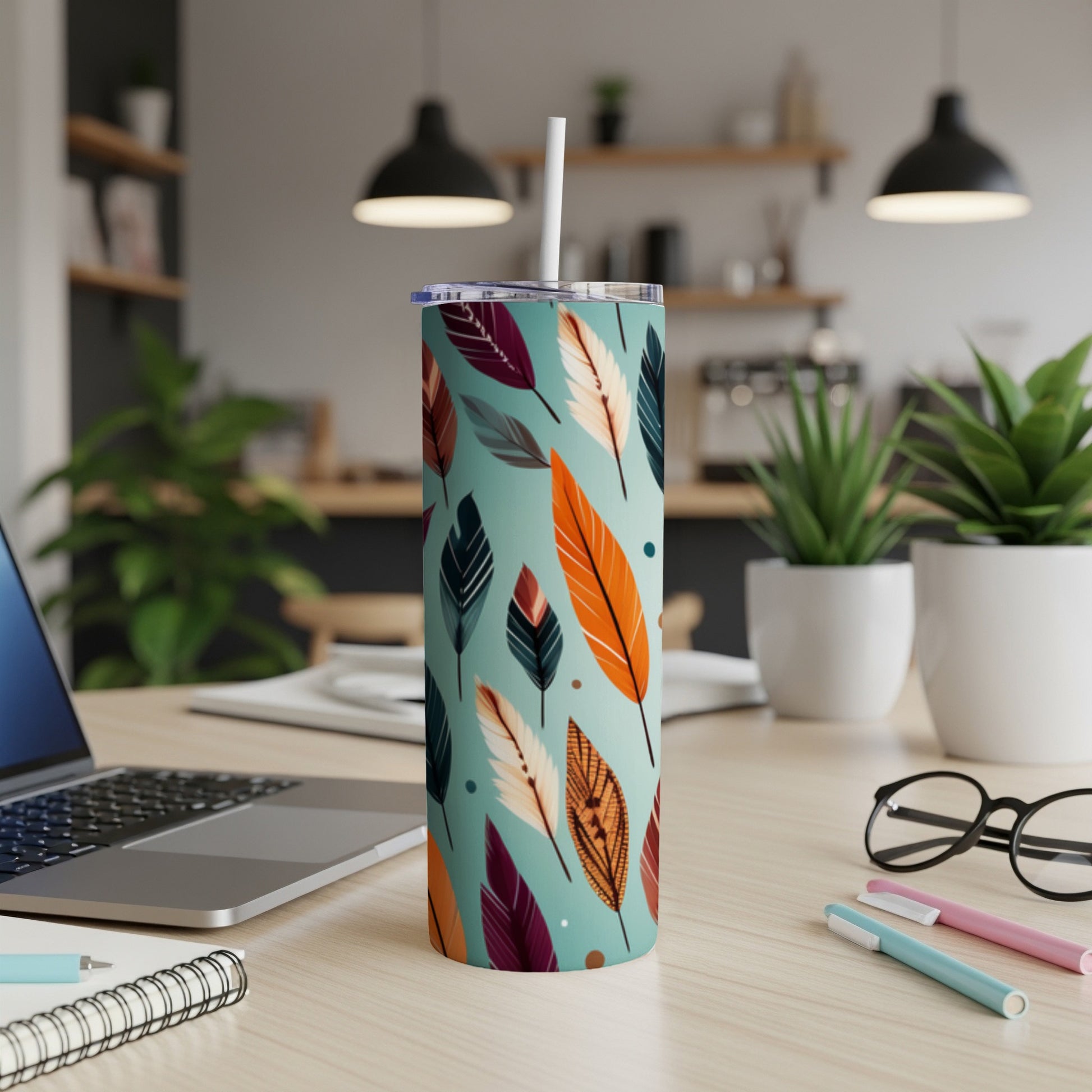 Turquoise tumbler with colorful feather pattern and straw, on a desk.