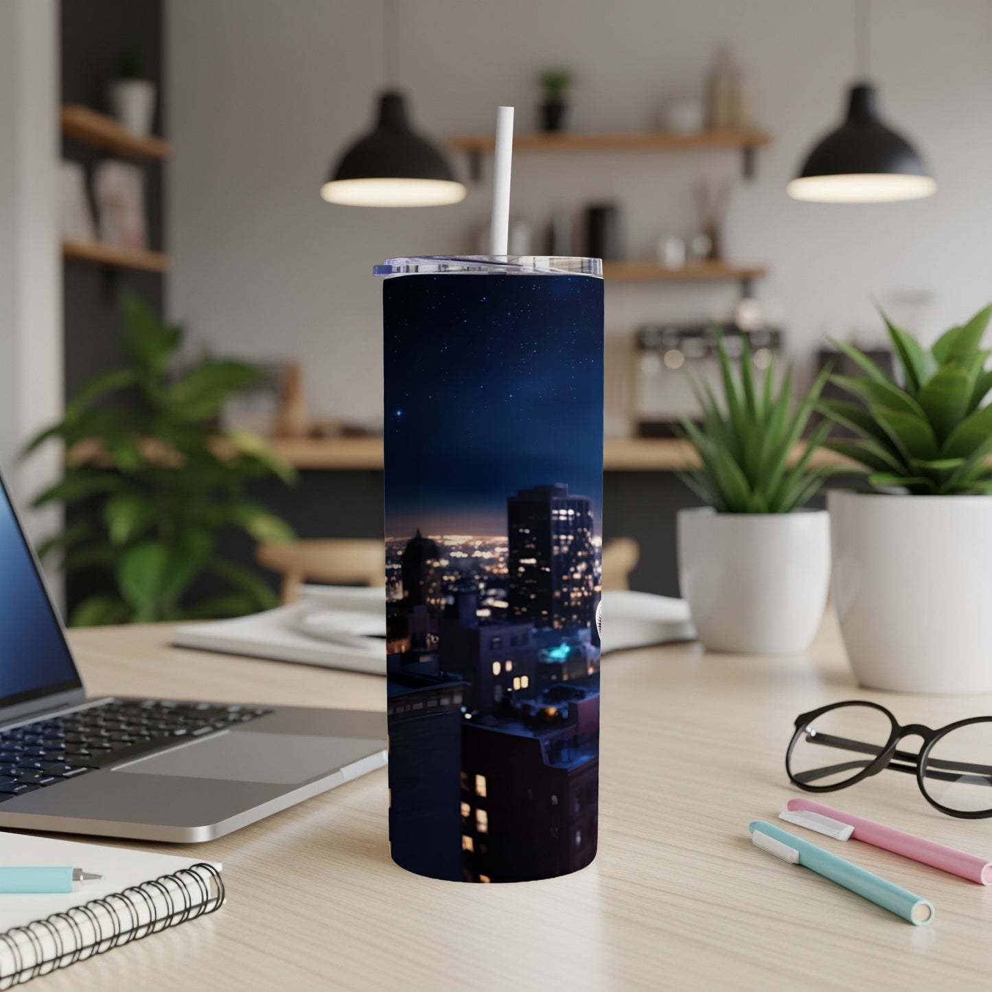 Tumbler with a nighttime city skyline print, straw in lid, on a desk.