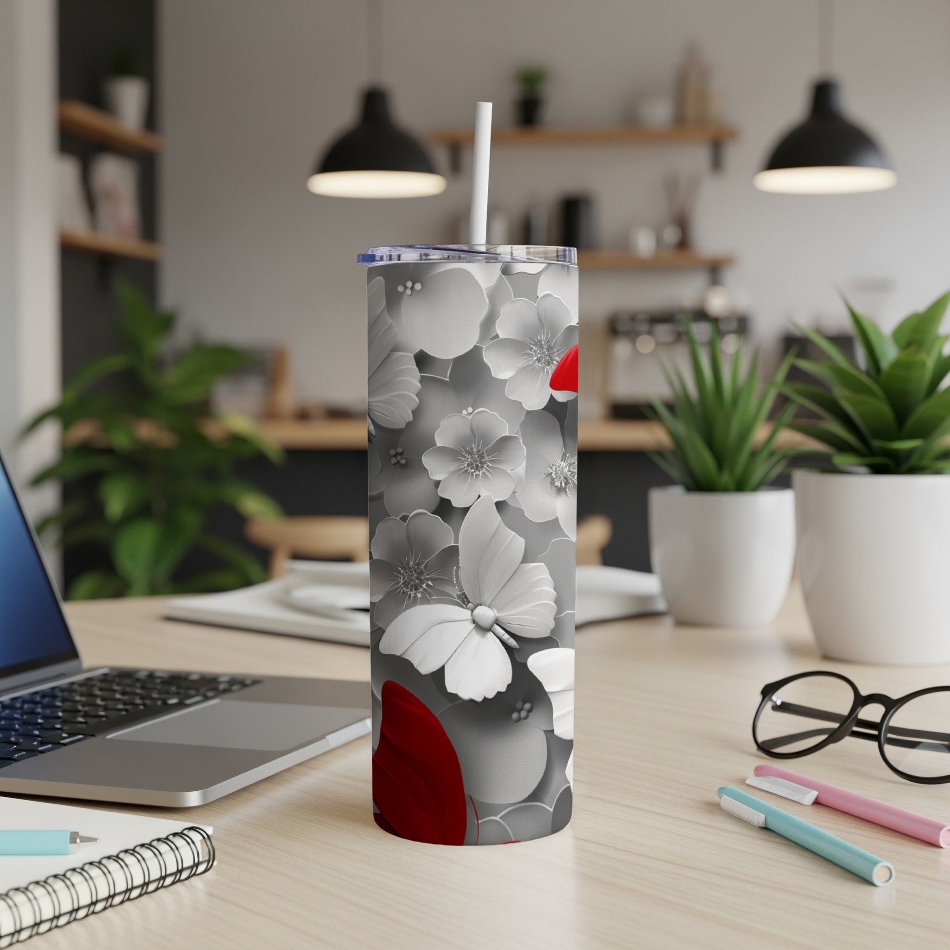 White floral tumbler with red accents and a straw, on a desk.