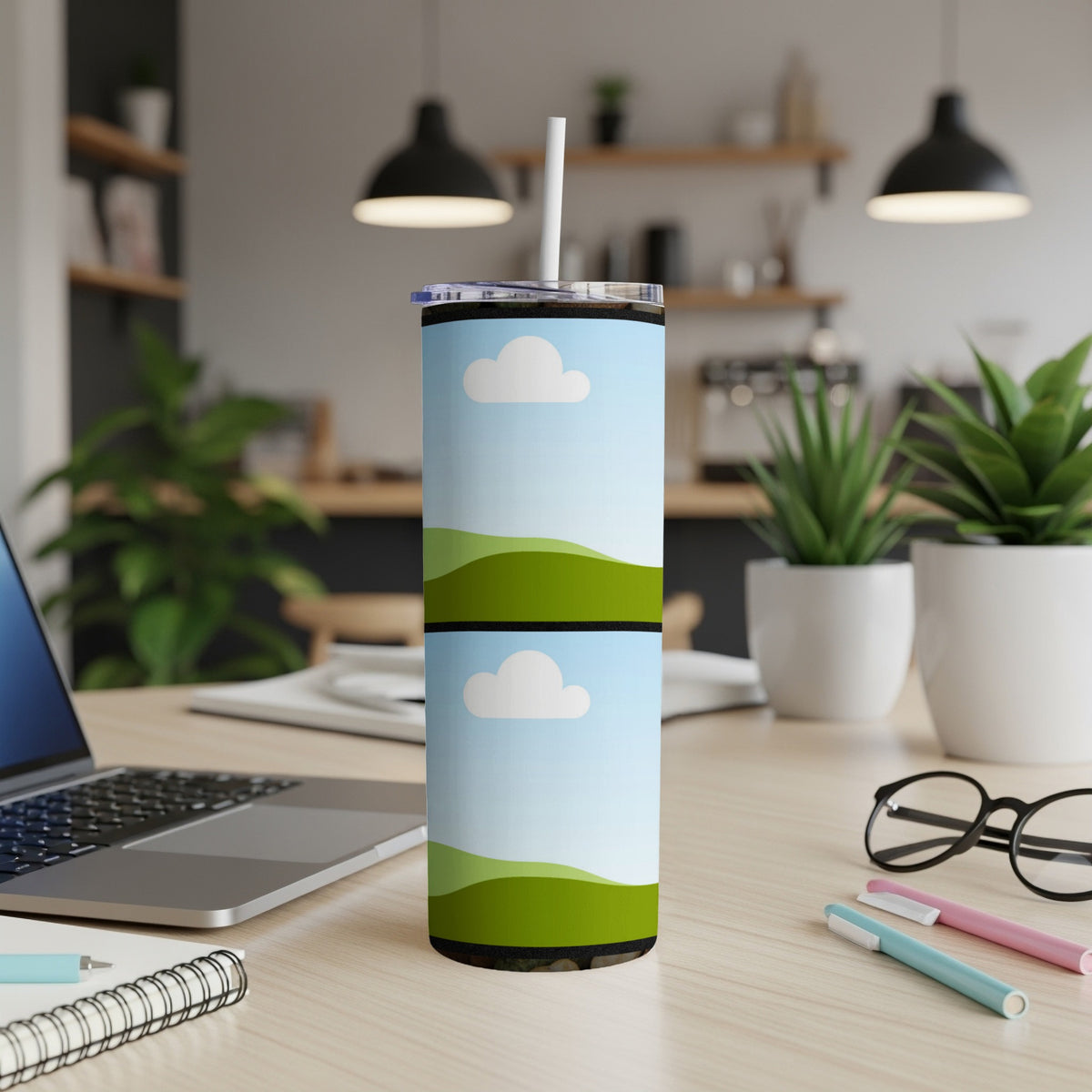 Tumbler with sky and green rolling hills design, on a desk.