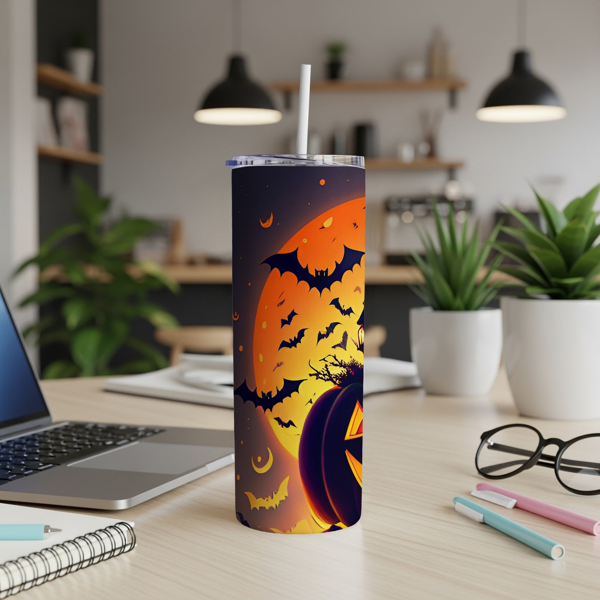 Halloween tumbler with bats, moon, and jack-o'-lantern on a desk.