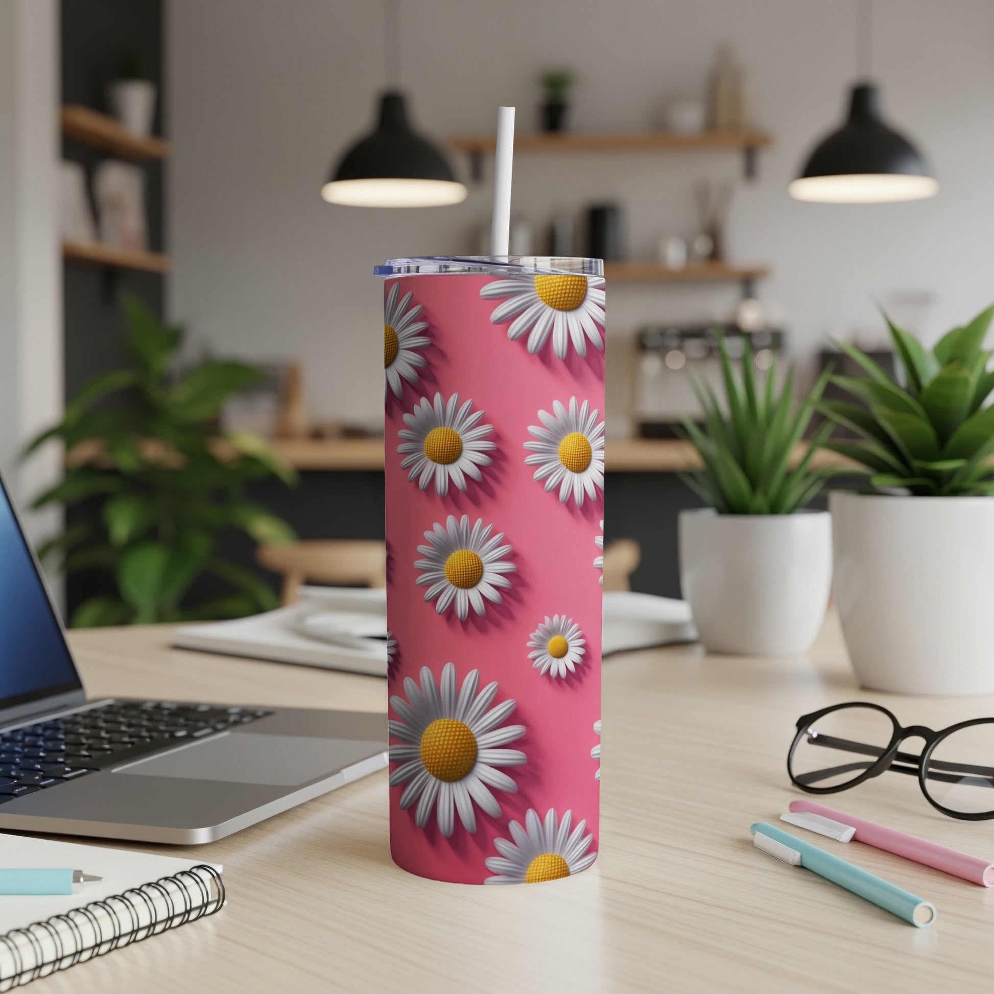 Pink tumbler with a repeating daisy pattern and straw, on a desk.
