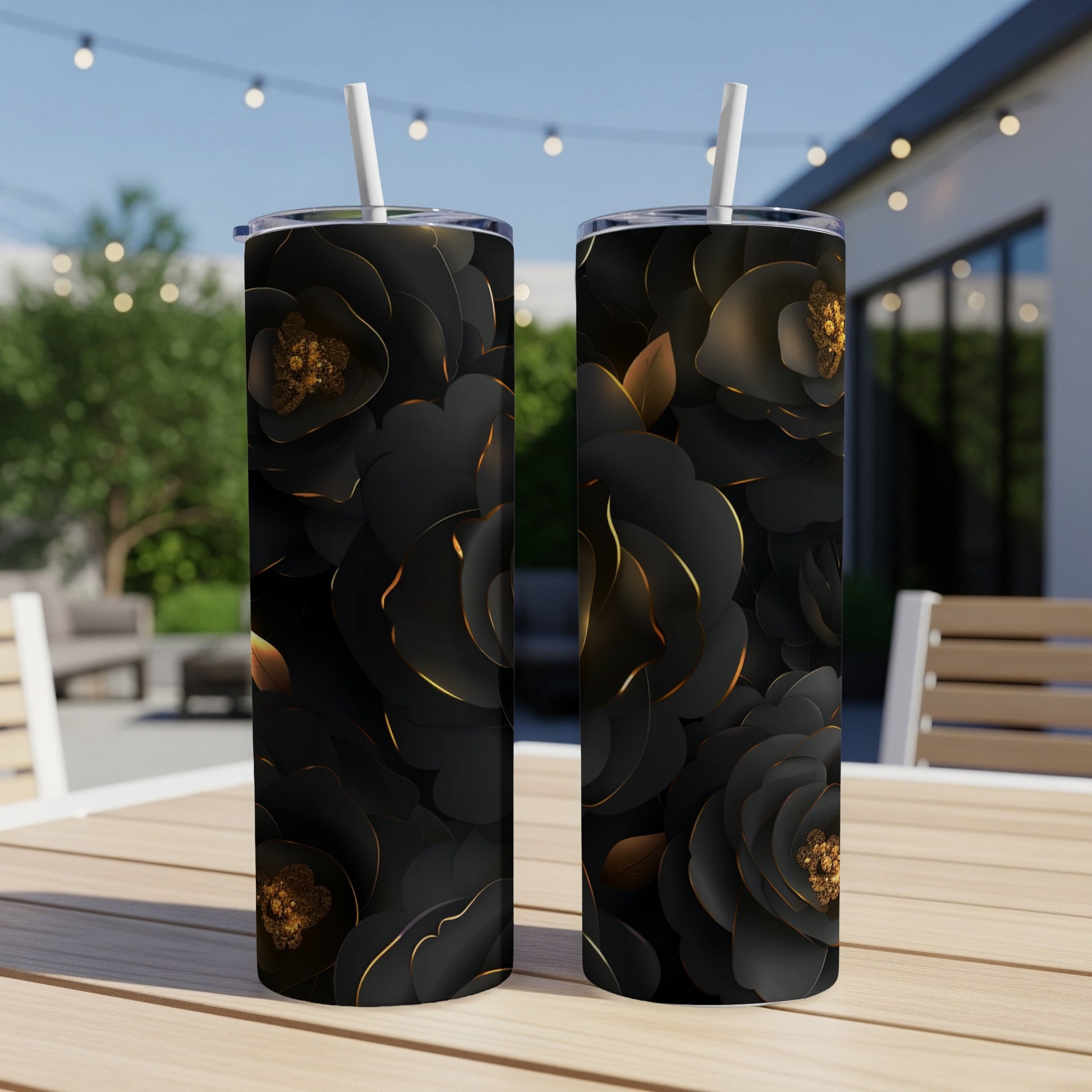 Two black tumblers with gold-edged rose designs sit on a wooden table outdoors.