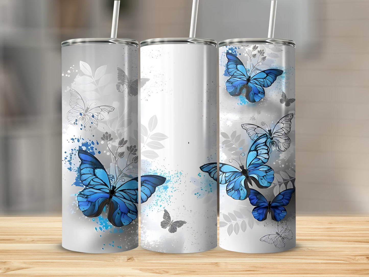 Three tumblers with blue butterflies and floral accents on a wooden surface.