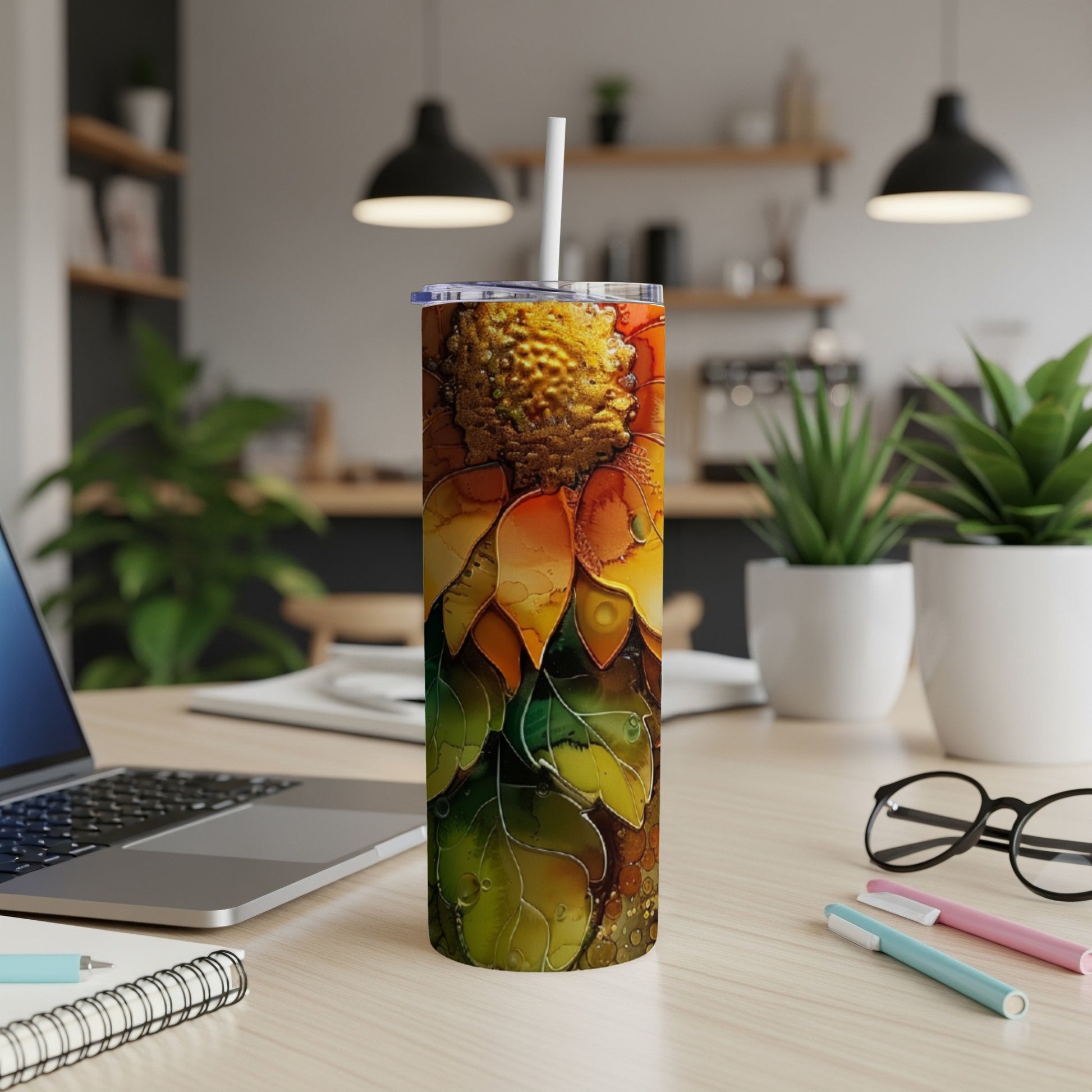 Sunflower tumbler with straw on a desk with laptop and pens.