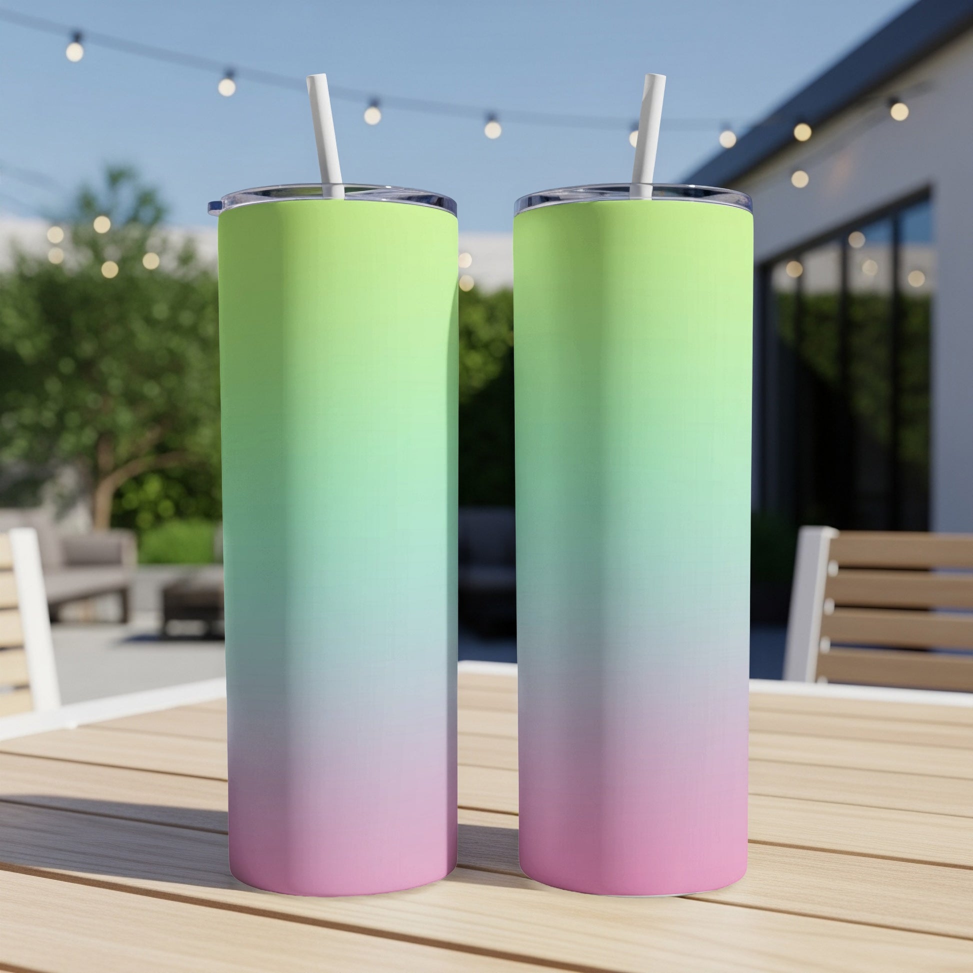 Two gradient tumblers, pink to green, with straws, on a wooden table outdoors.