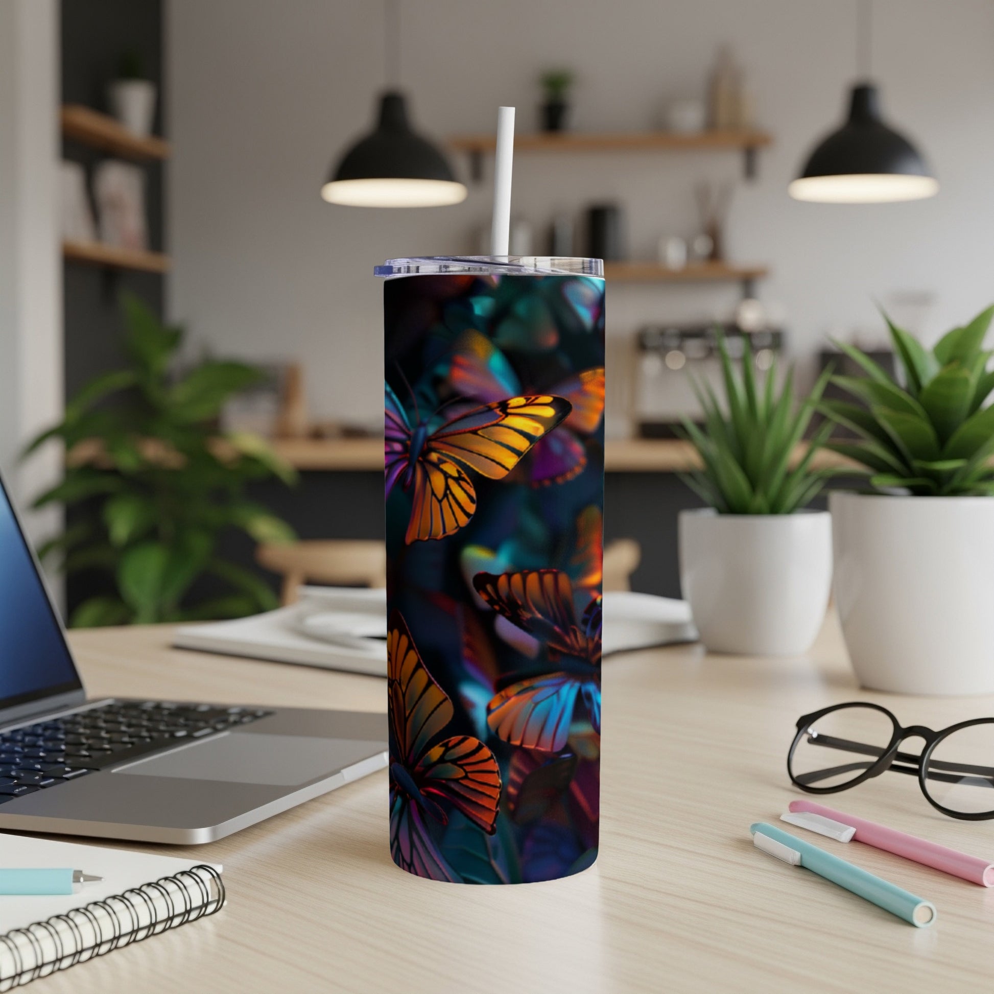 Tumbler with colorful butterfly pattern on a desk with a laptop and pens.