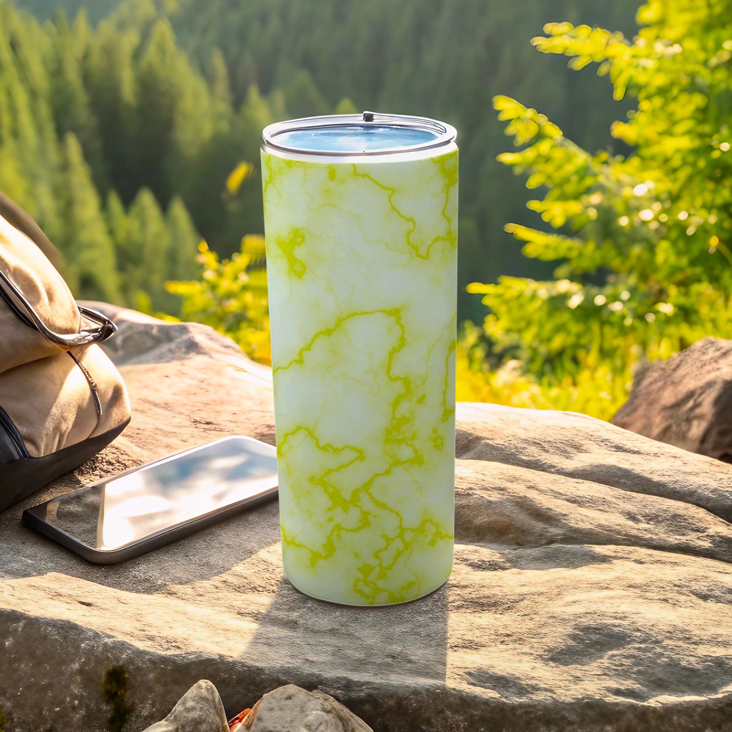 Green and white marbled tumbler with phone and backpack on rocks.
