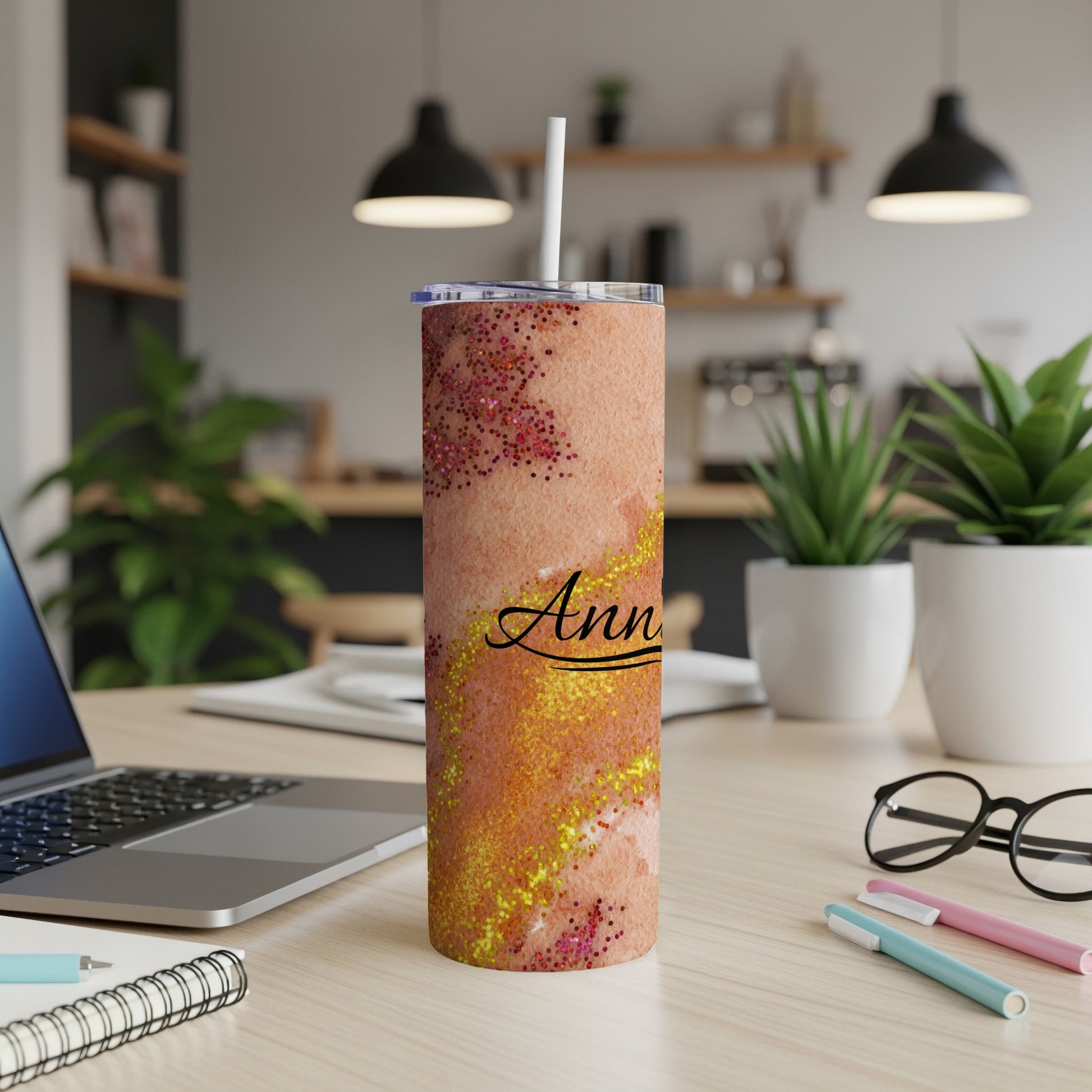 Glittery tumbler with "Ann" text on desk with laptop and plants.