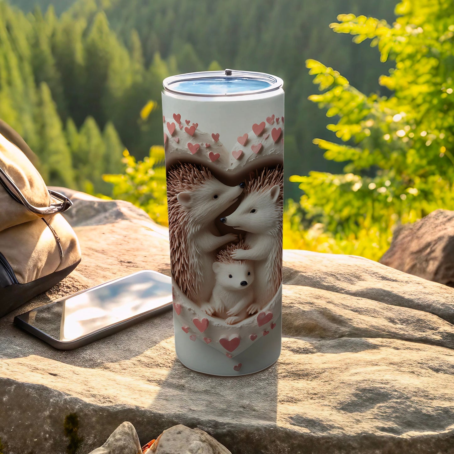 Hedgehog family inside hearts on a white tumbler, outdoors with phone and bag.