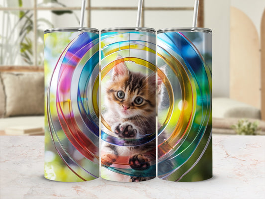 Kitten peeking through colorful concentric circles on a tumbler.