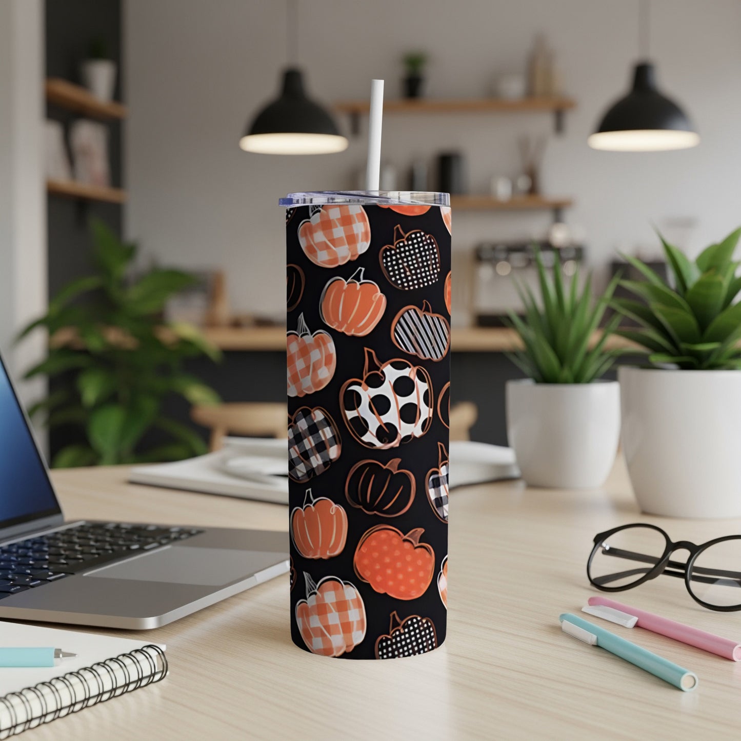 Tall tumbler with pumpkin pattern and white straw on a desk.