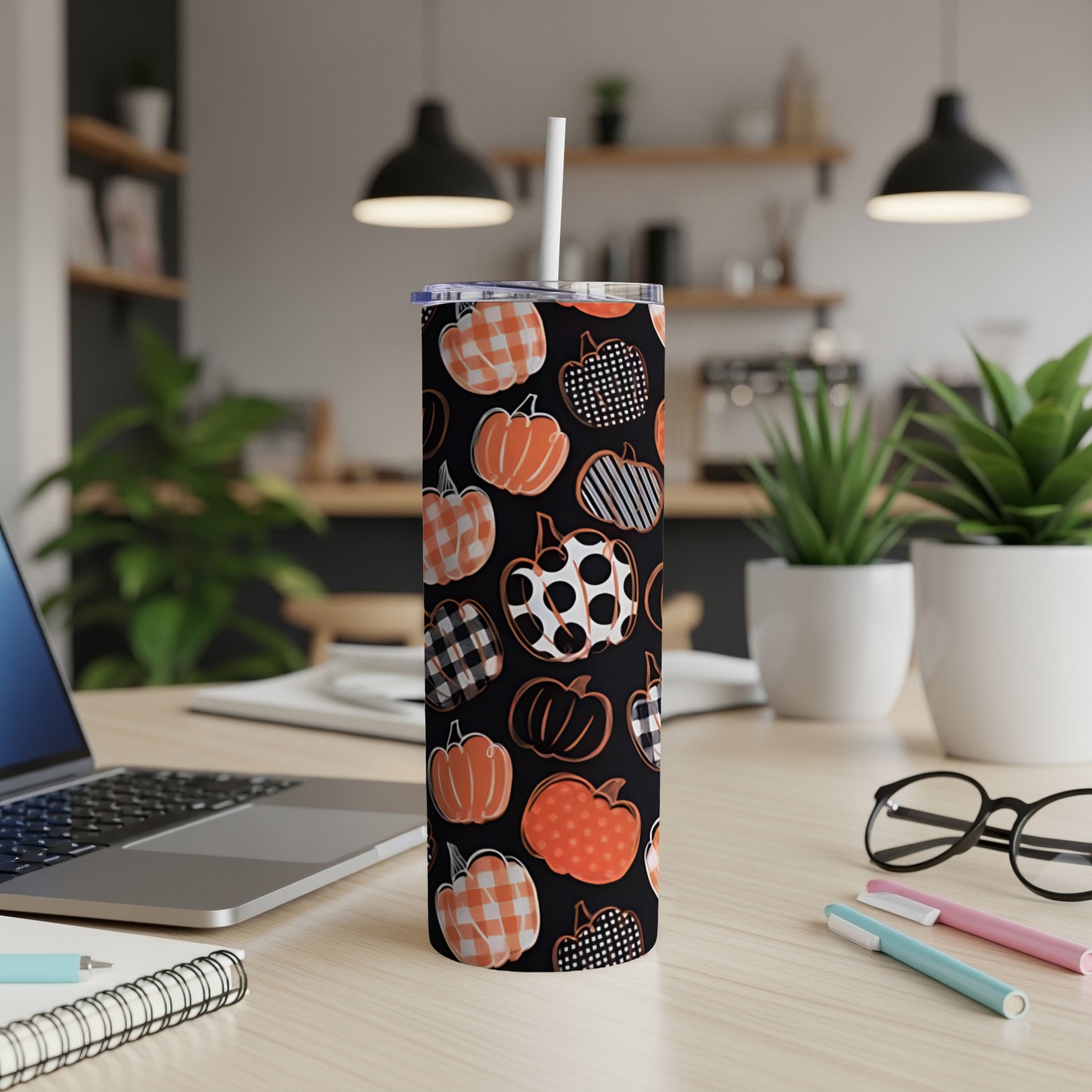 Tall tumbler with pumpkin pattern and white straw on a desk.
