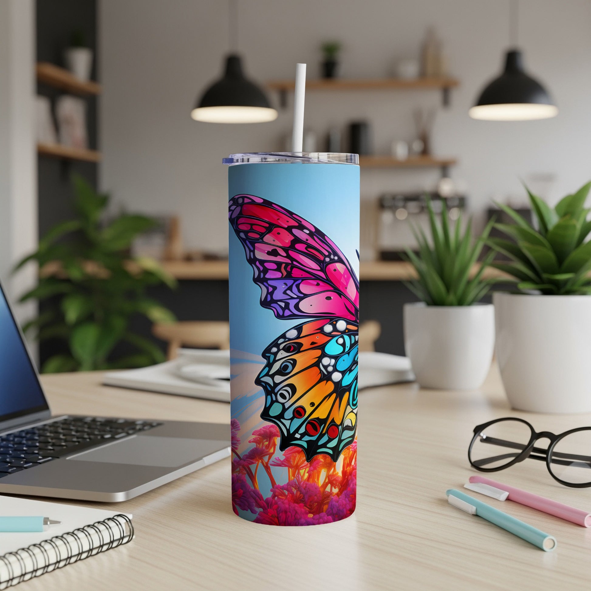 Tall tumbler with colorful butterfly design on desk with laptop and pens.