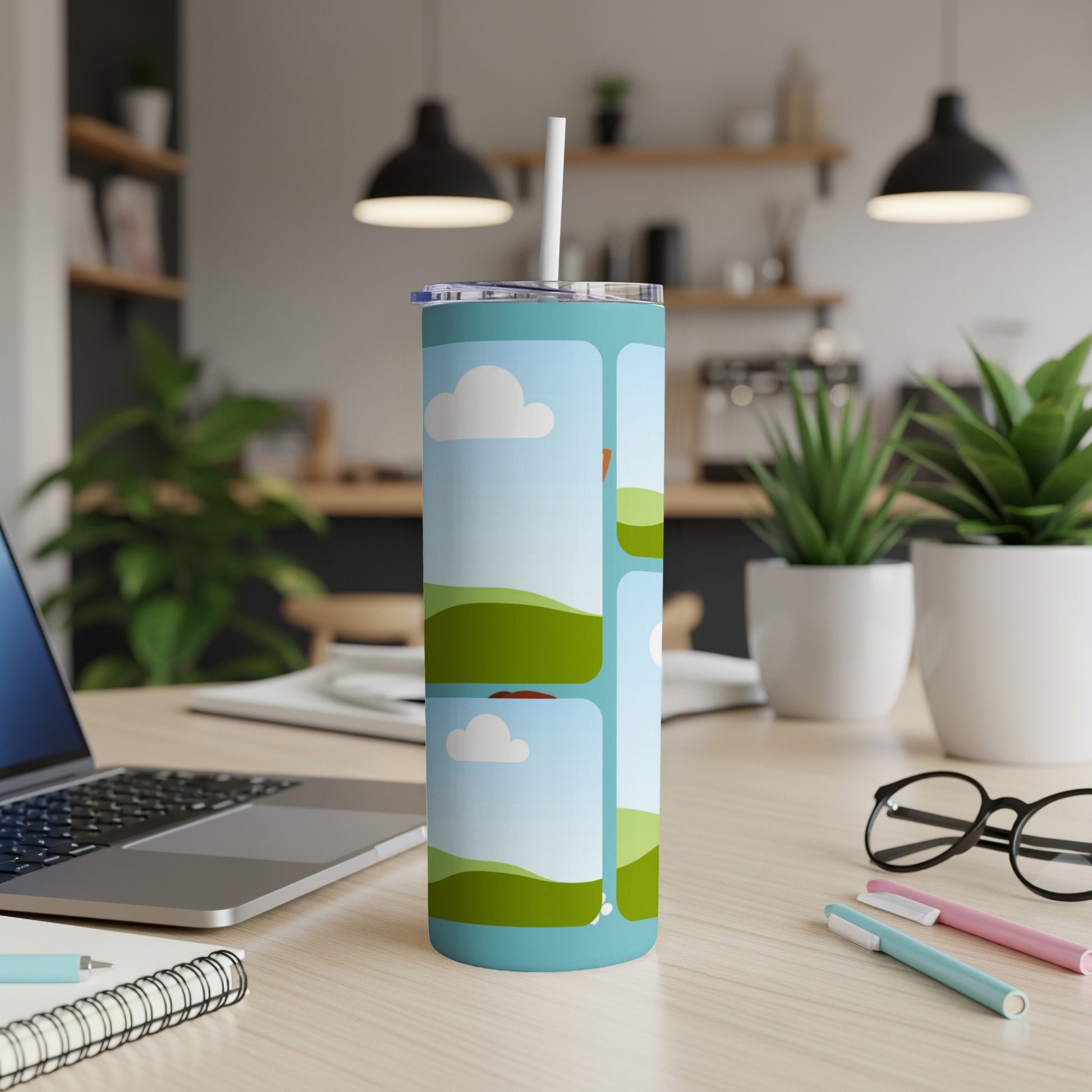 Turquoise tumbler with a cartoon landscape print and straw on a wooden desk.