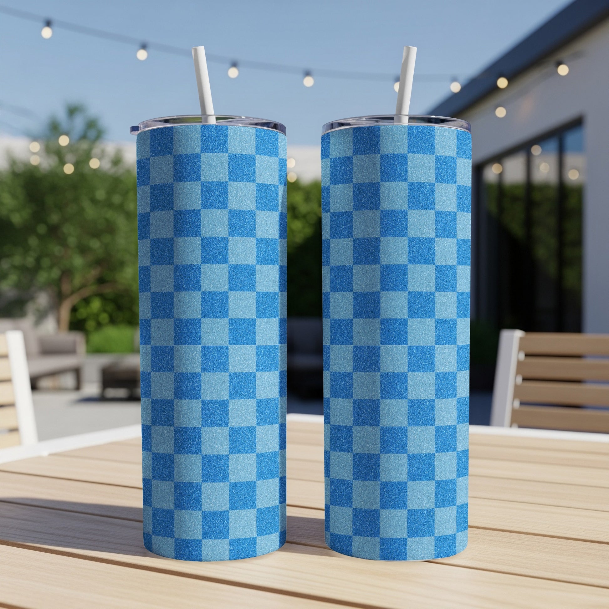 Two blue checkered tumblers with straws on a wooden table.