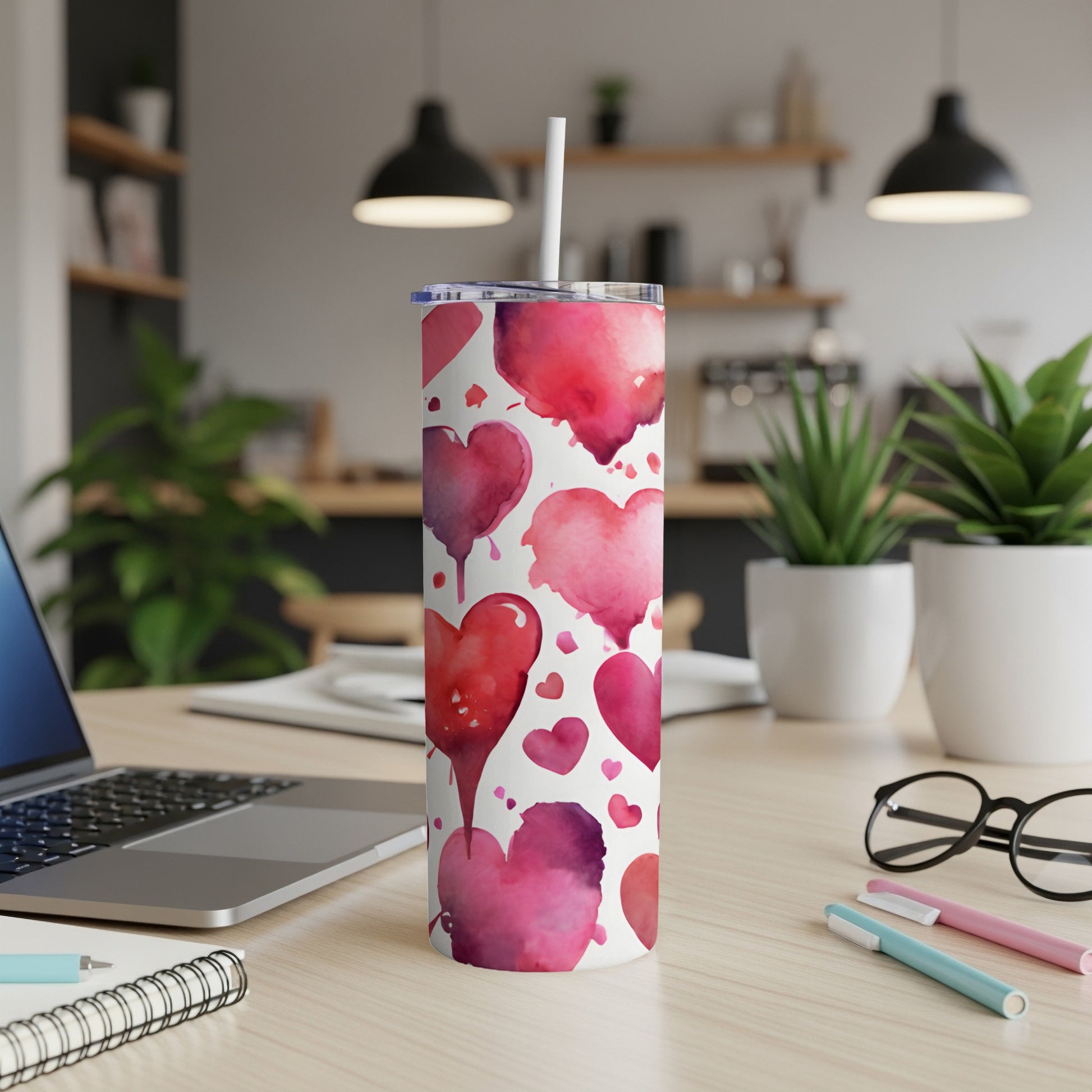 White tumbler with watercolor hearts pattern and straw on a desk.
