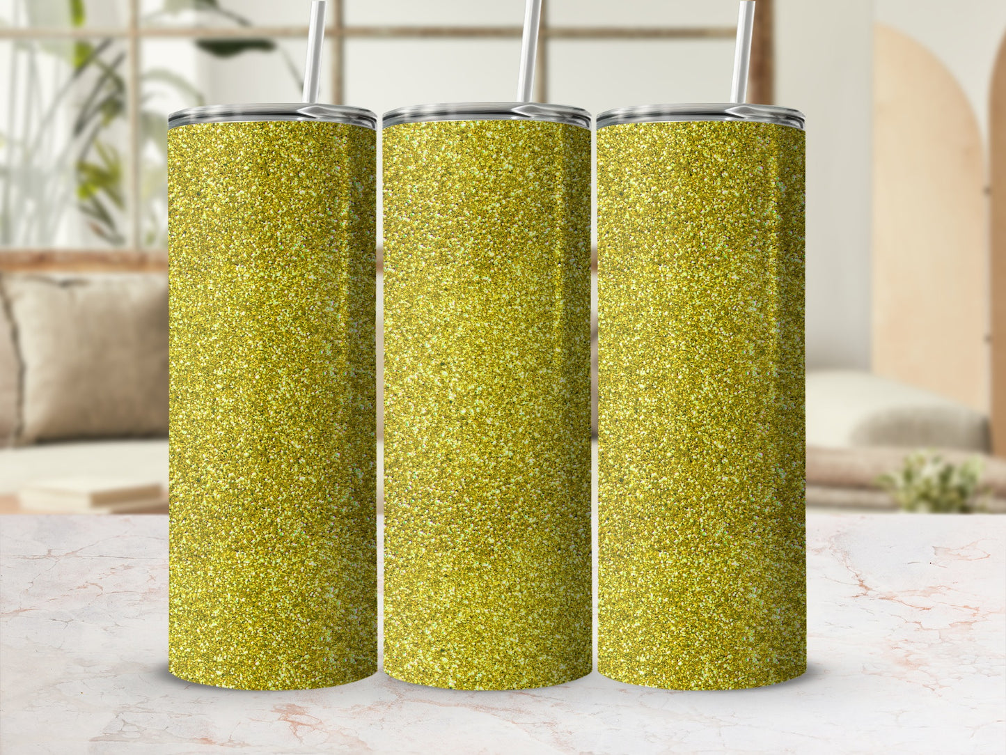 Three gold glitter tumblers with straws displayed together on a marble surface.