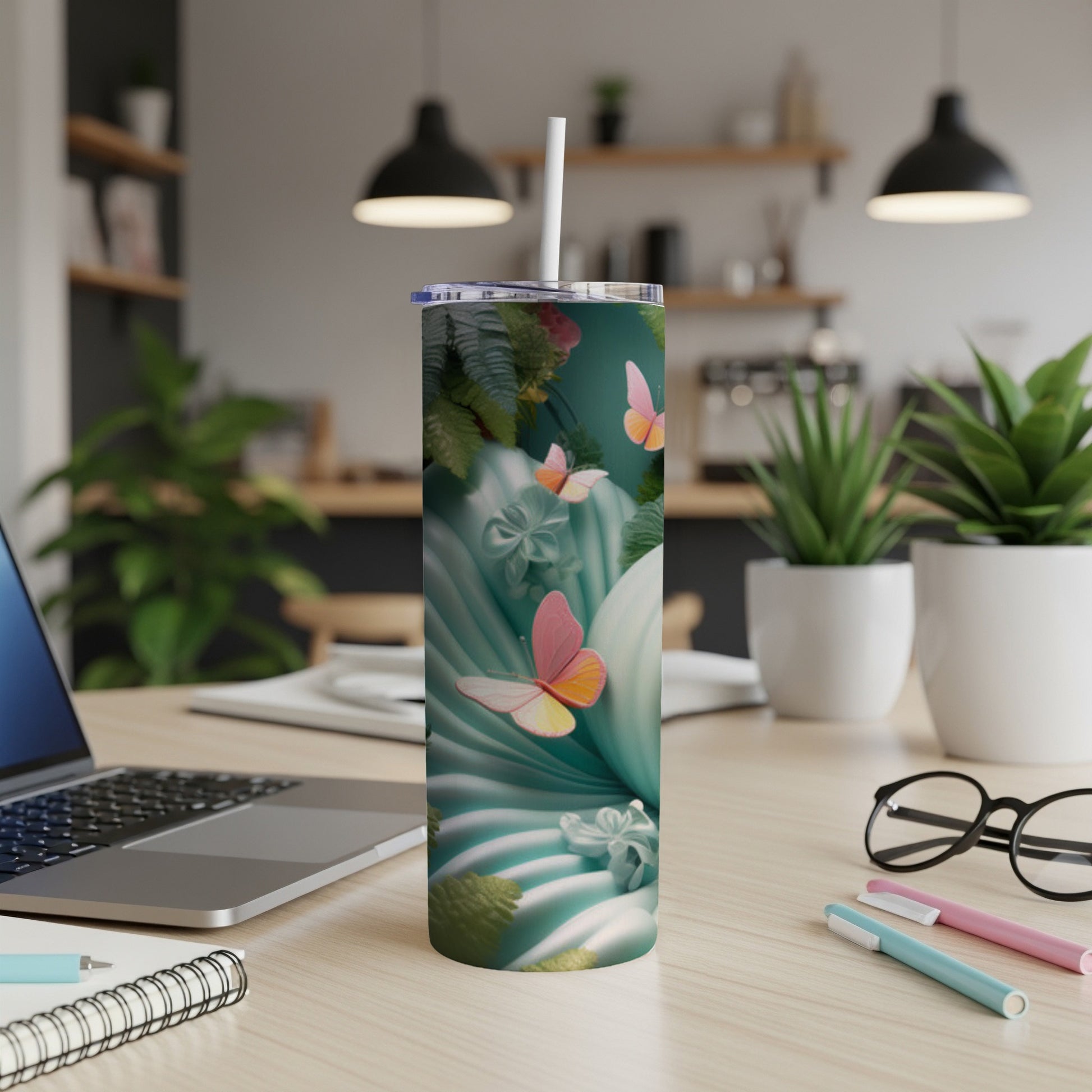 Teal tumbler with butterflies and tropical leaves, on a desk.
