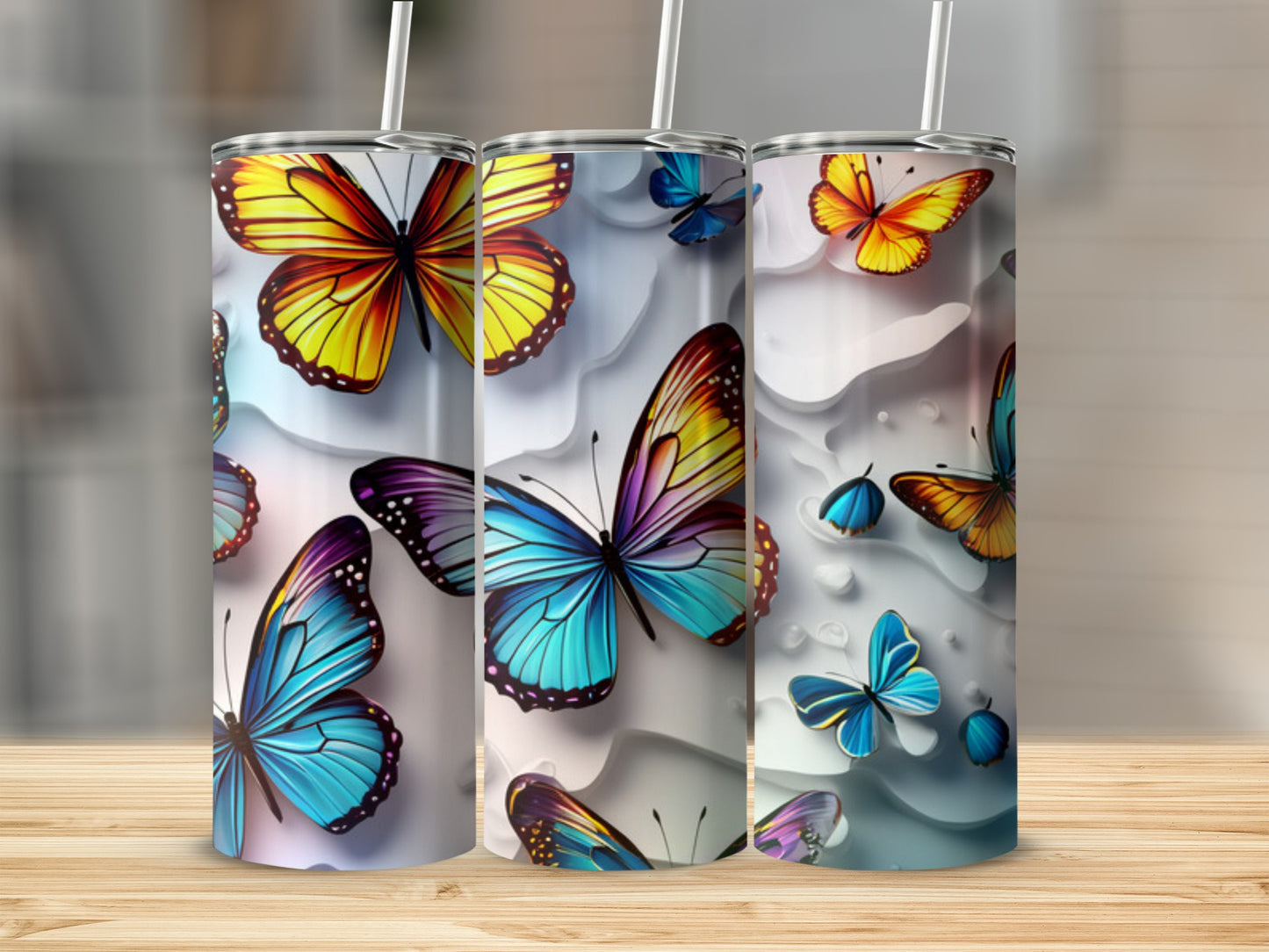 Three tumblers with colorful butterfly designs on a wooden surface.