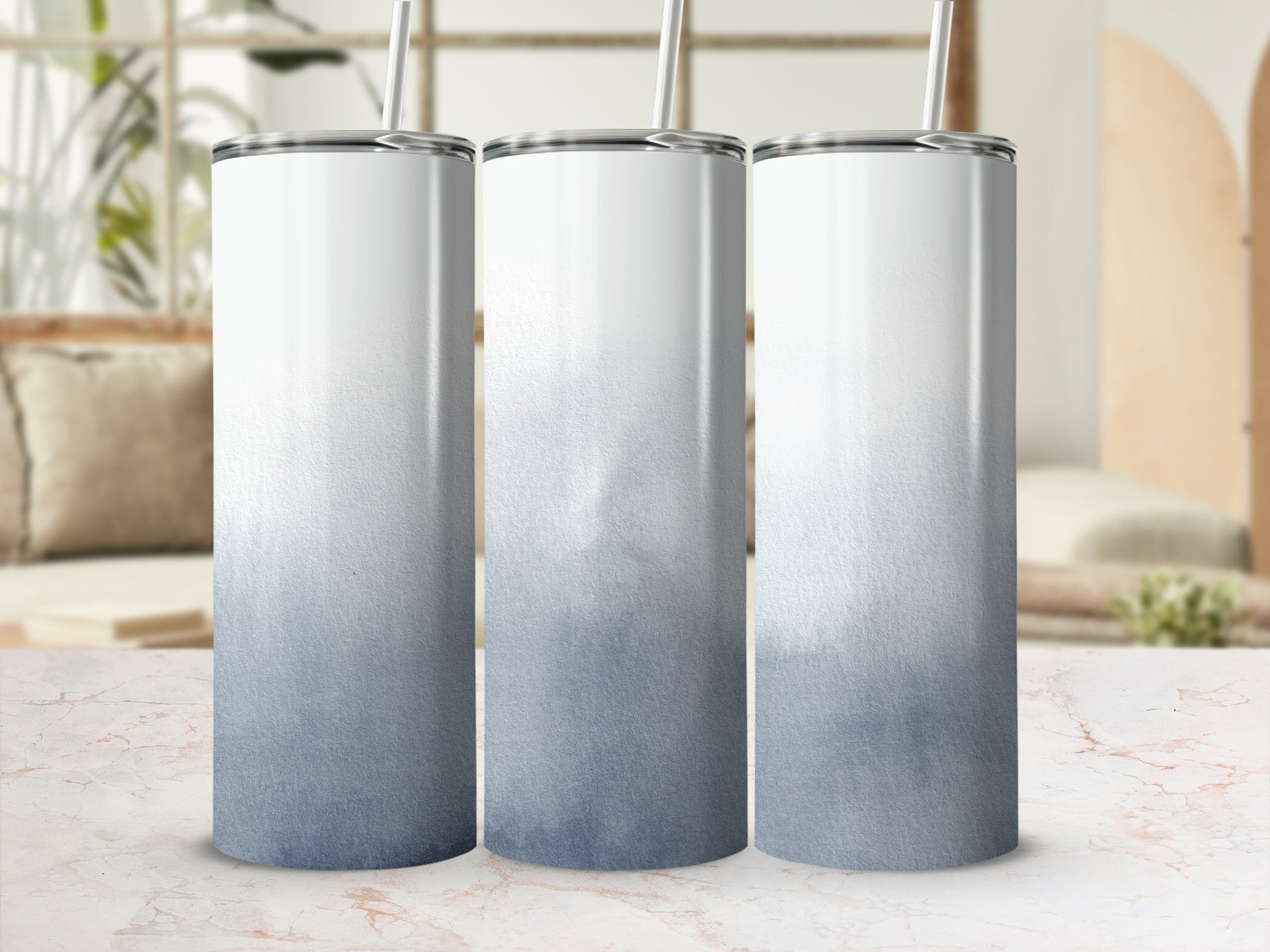 Three blank white and blue ombre tumblers with straws on a counter.