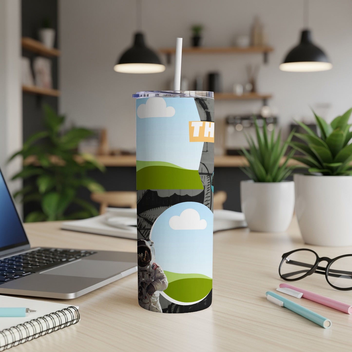 Tall tumbler with an astronaut graphic and "TH" text on a desk.
