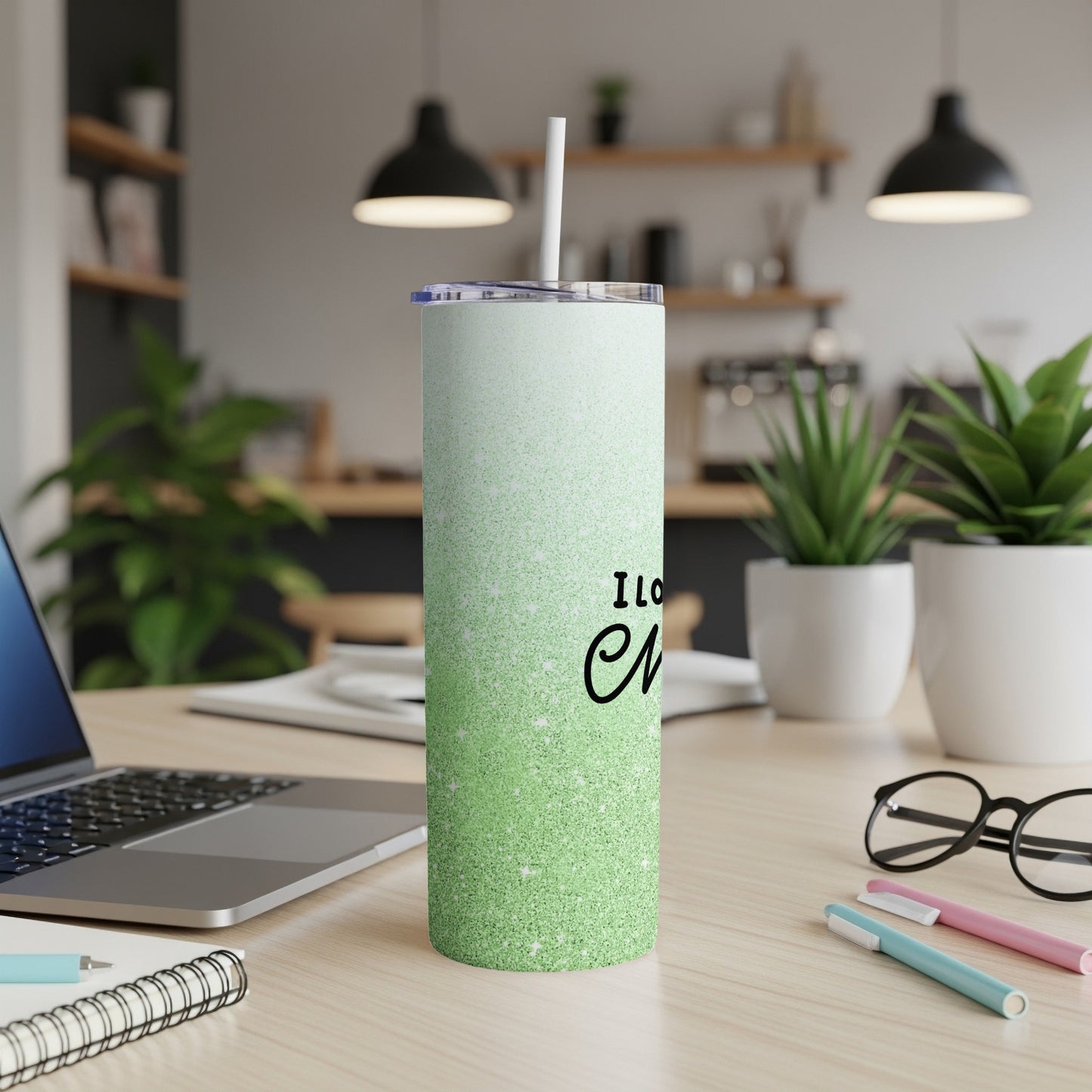 Green glitter tumbler with "I love..." text, on a desk with a laptop.