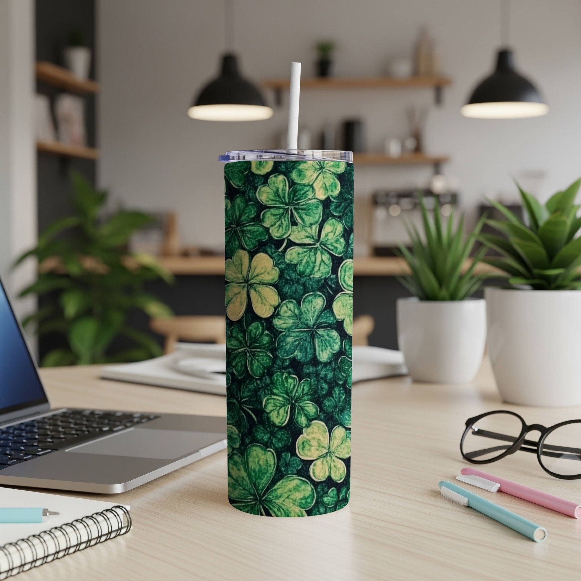 Green tumbler with clover pattern and straw, on a desk.