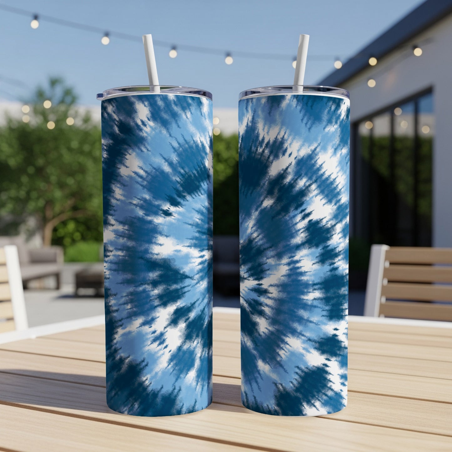 Two blue and white tie-dye stainless steel tumblers with straws on a table.