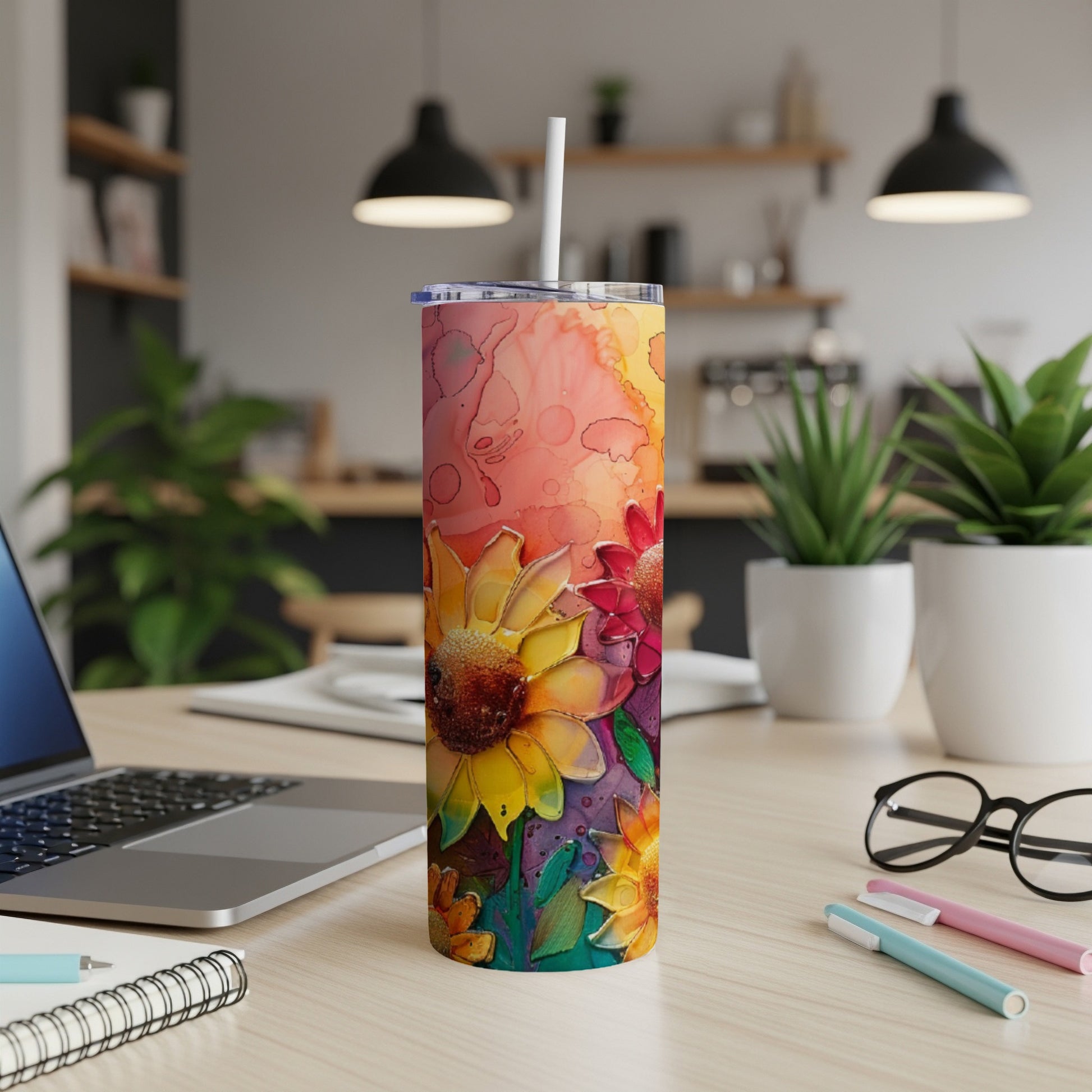 Floral tumbler with straw on a desk with a laptop and pens.