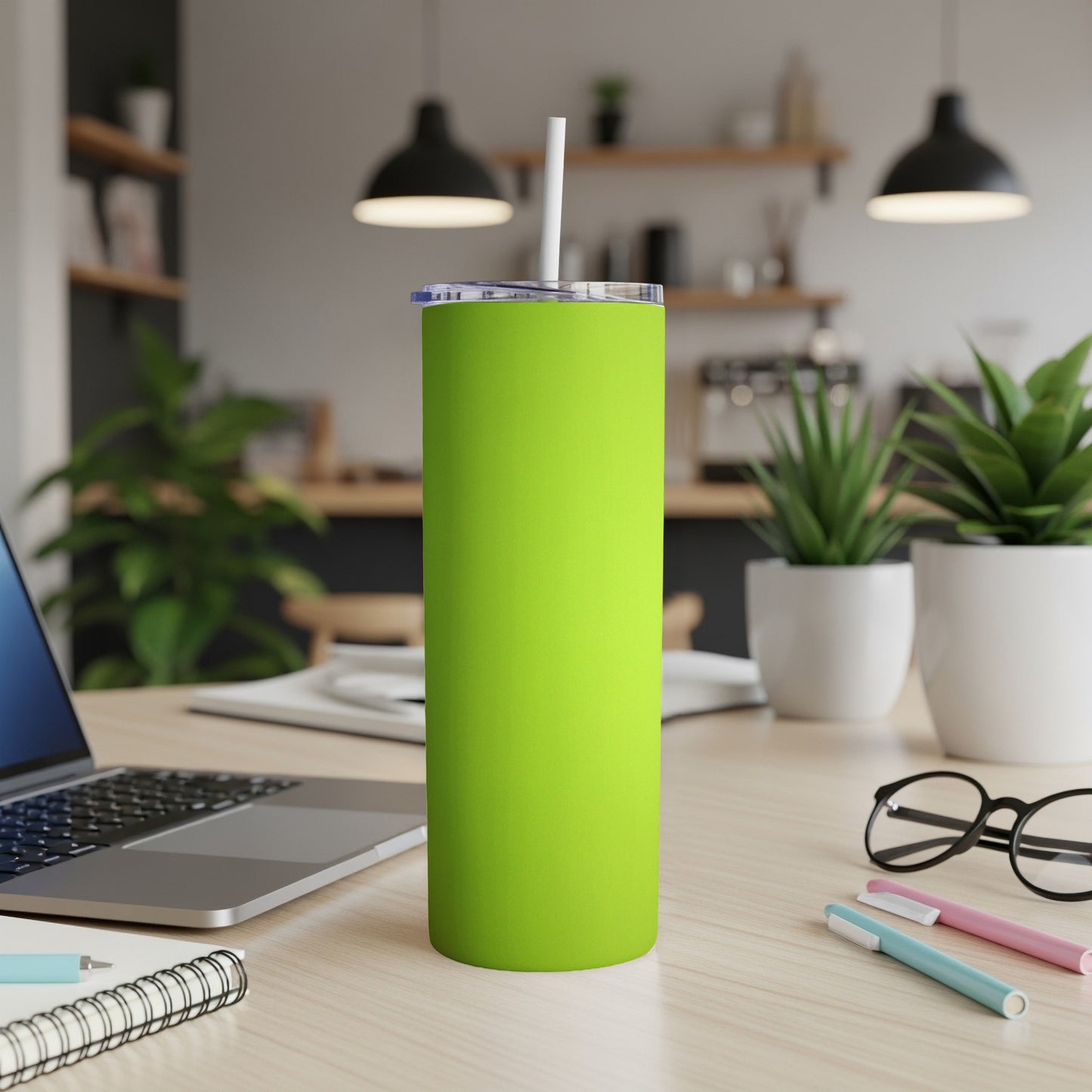 Green tumbler with a white straw on a desk with a laptop and notebooks.