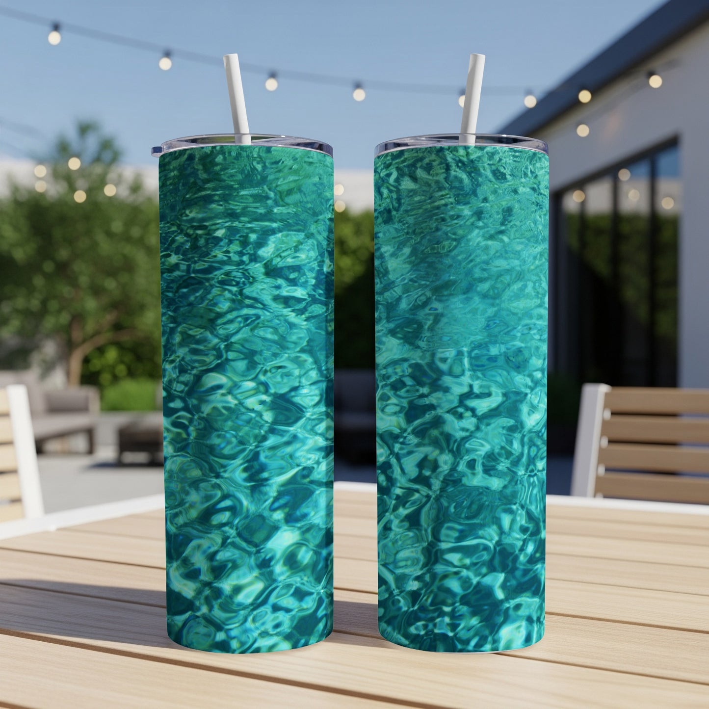 Two tumblers with a rippling turquoise water design sit on a wooden table outdoors.