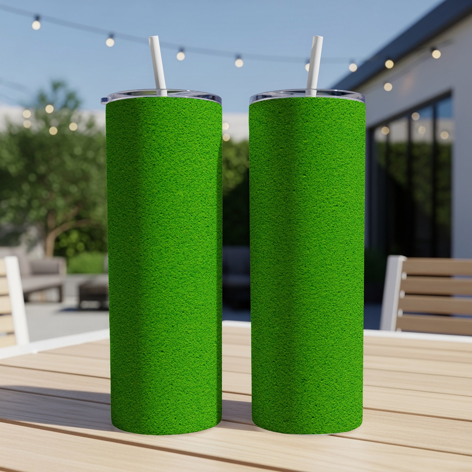 Two green tumblers with white straws stand on a wooden table outdoors.