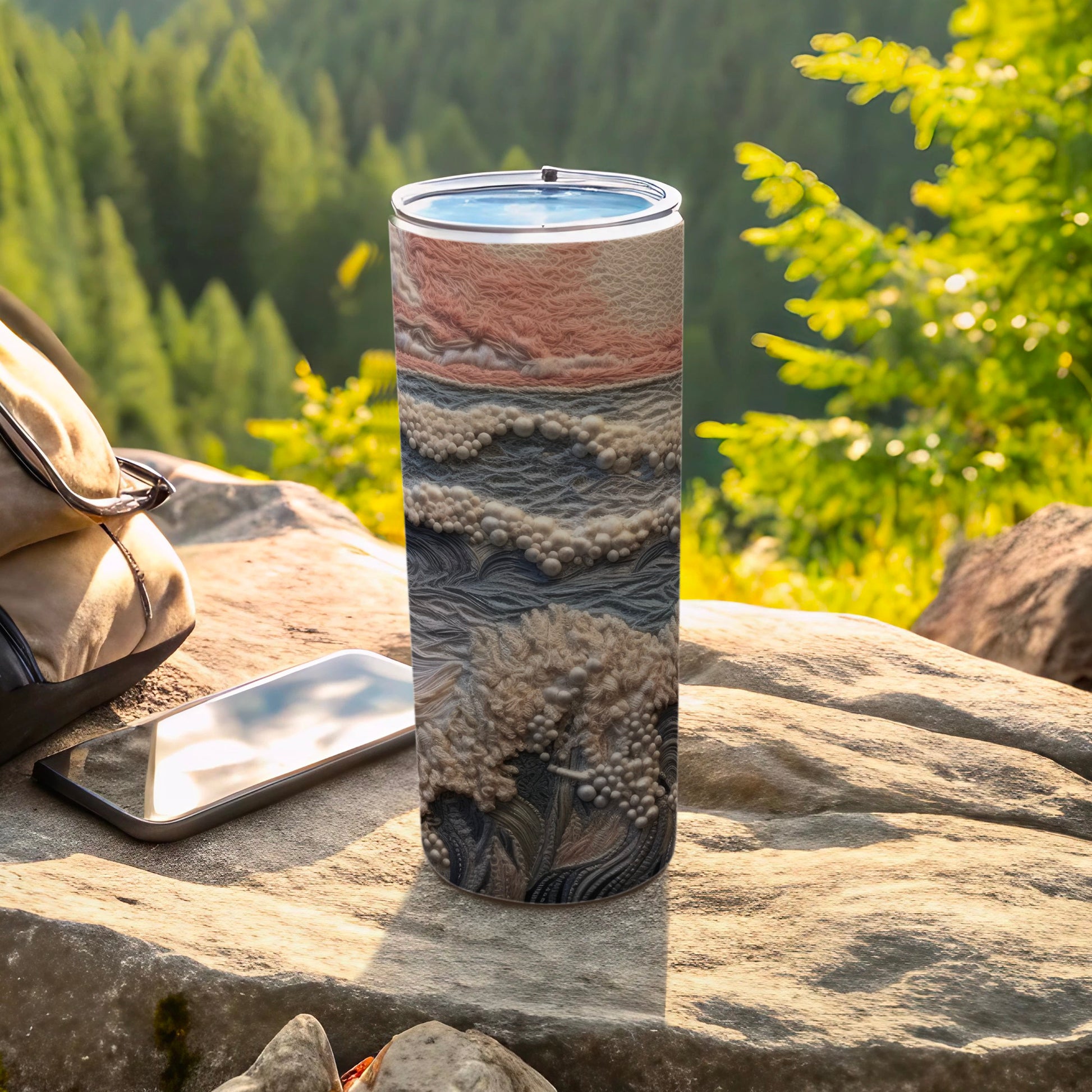 Tumbler with textured, abstract design on a rock outdoors.