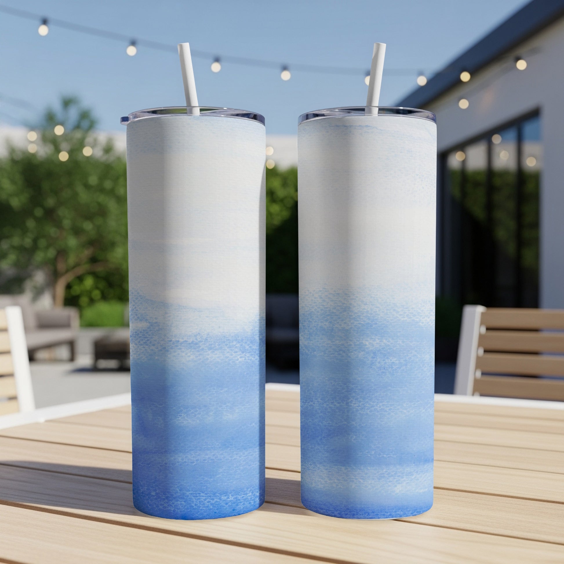 Two blue and white gradient tumblers with straws on a table.