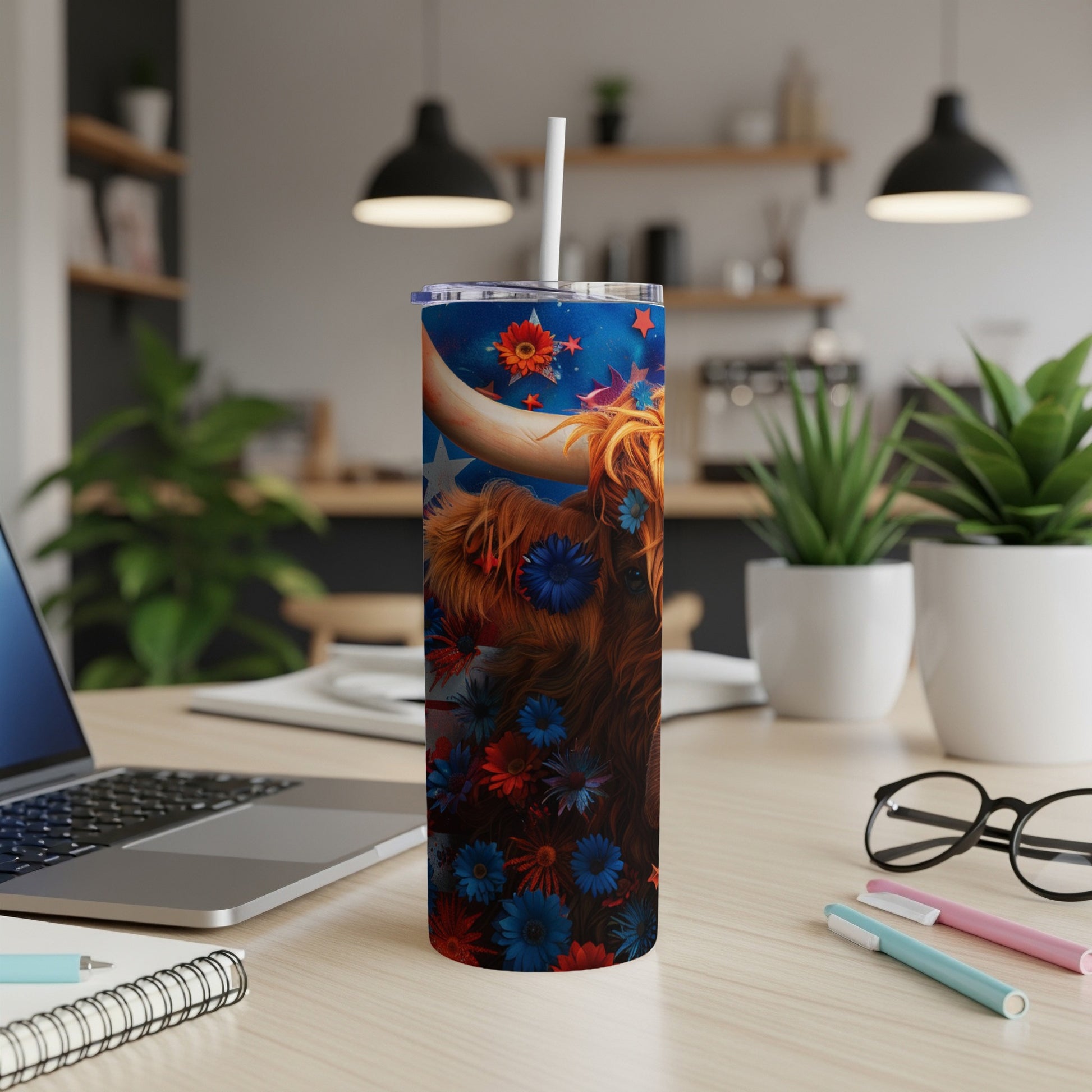 Highland cow tumbler with patriotic floral design, white straw, on desk.