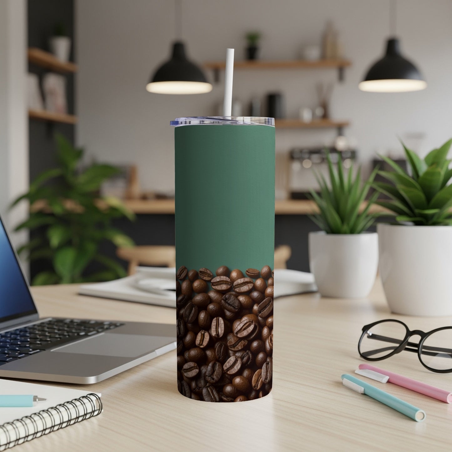Green tumbler with coffee beans on a desk with a laptop and pens.
