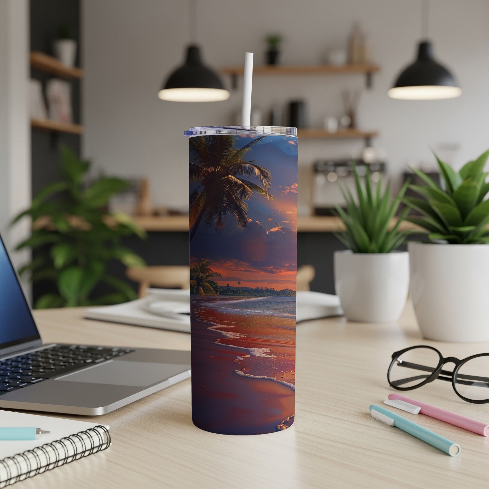 Tall tumbler with sunset beach scene and straw on desk.