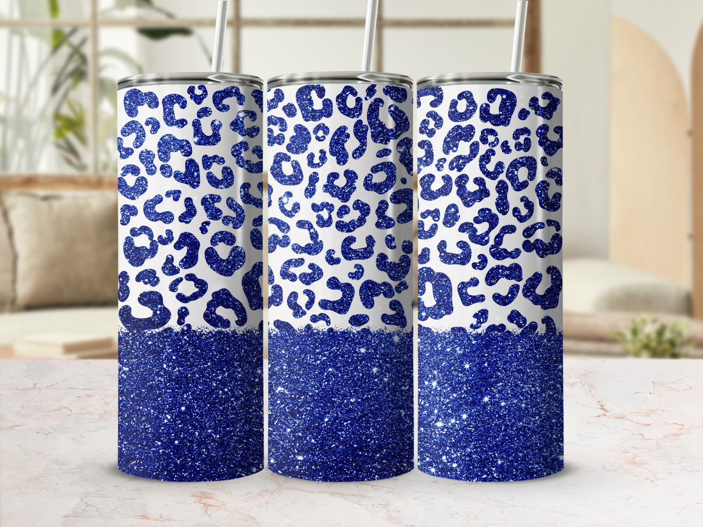 Three blue glitter leopard print tumblers with straws on a marble surface.
