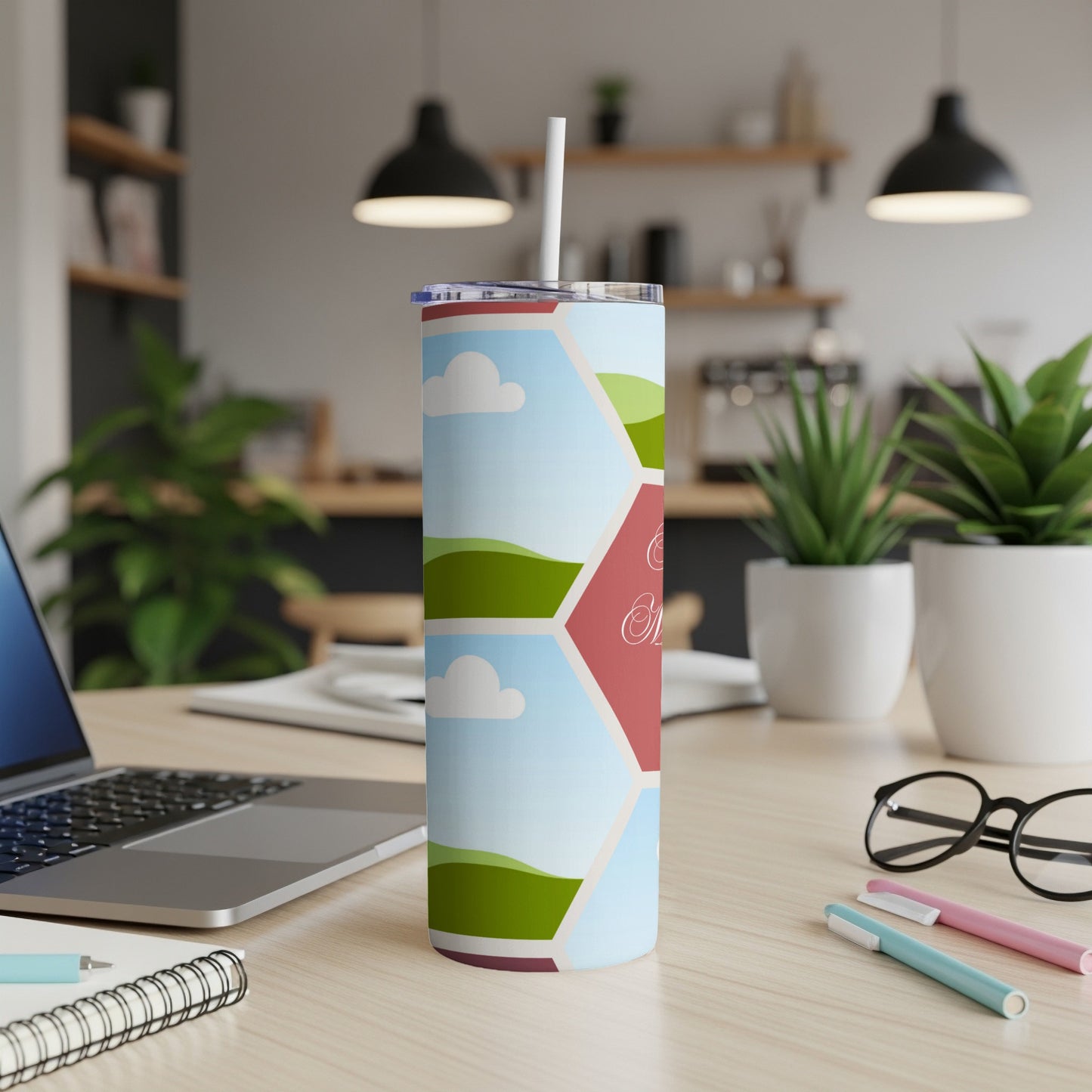 Tumbler with hexagonal landscape design and cursive text on a desk.