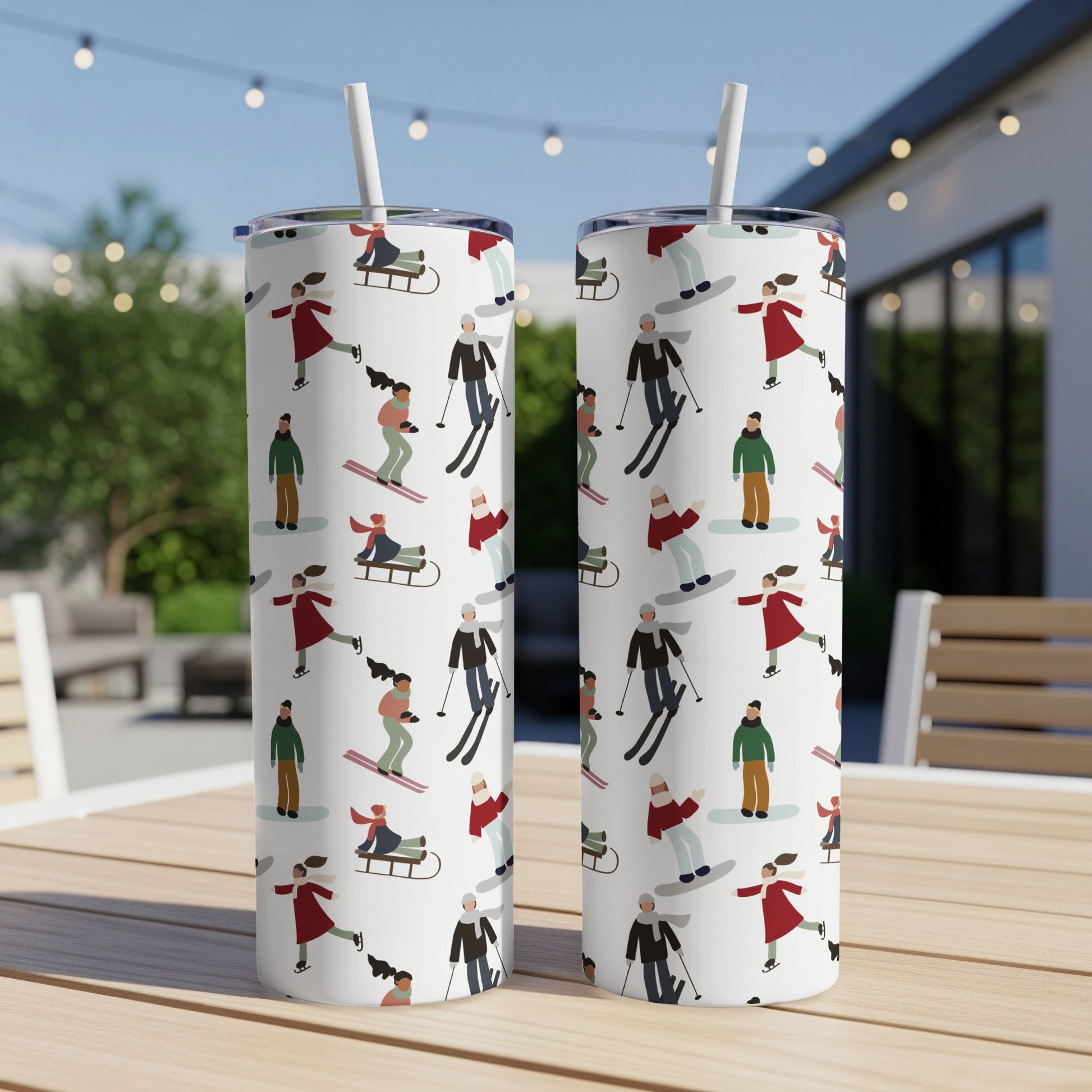 Two white tumblers with a pattern of skiers and snowboarders on an outdoor table.
