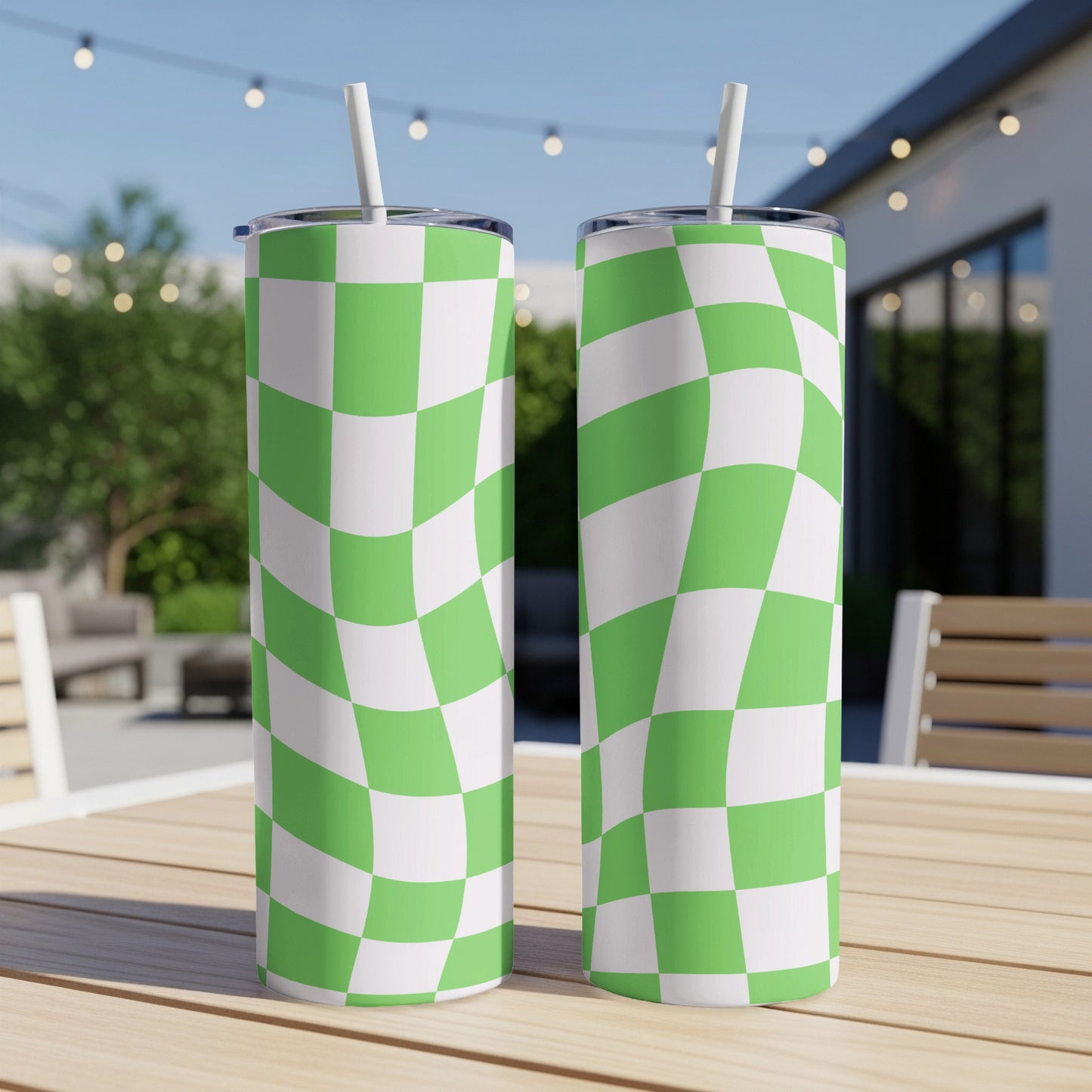Two green and white checkered tumblers with straws on a wooden table outdoors.