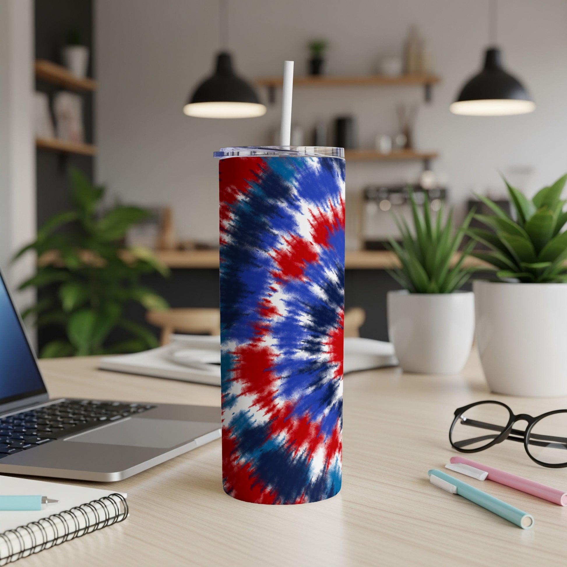 Red, white, and blue tie-dye tumbler with straw on a desk.