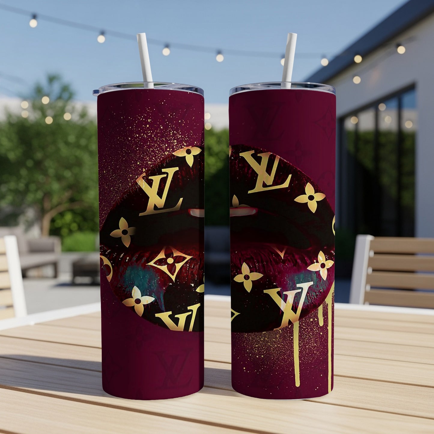 Two burgundy tumblers with gold lips and pattern on a wooden table outside.
